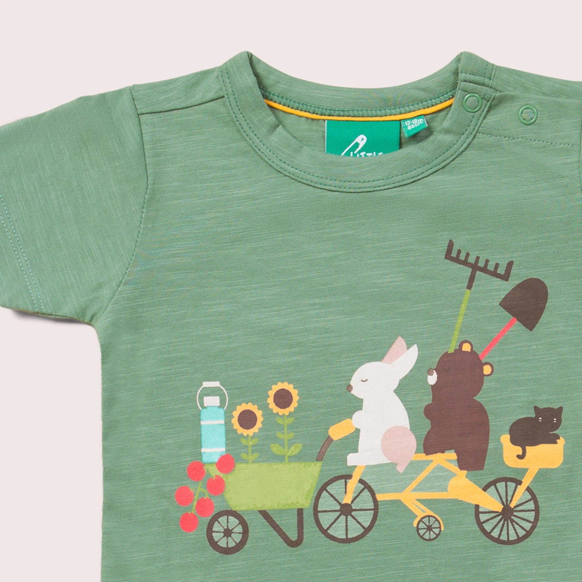 Sage green toddler t-shirt featuring a rabbit, bear, and cat riding a tandem bicycle with a wheelbarrow of sunflowers and