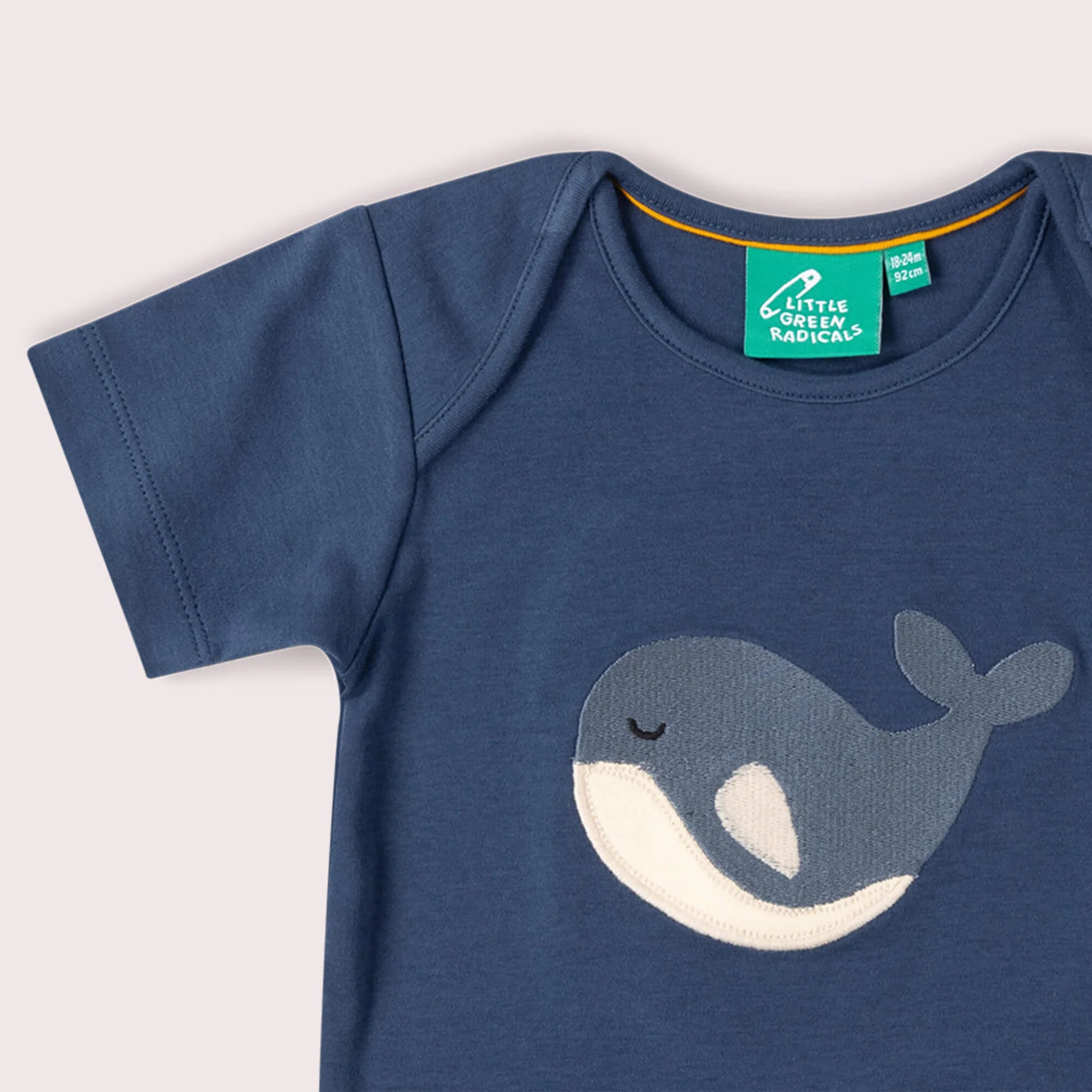 Blue baby shirt with whale design and Little Green Radicals tag on a light gray background