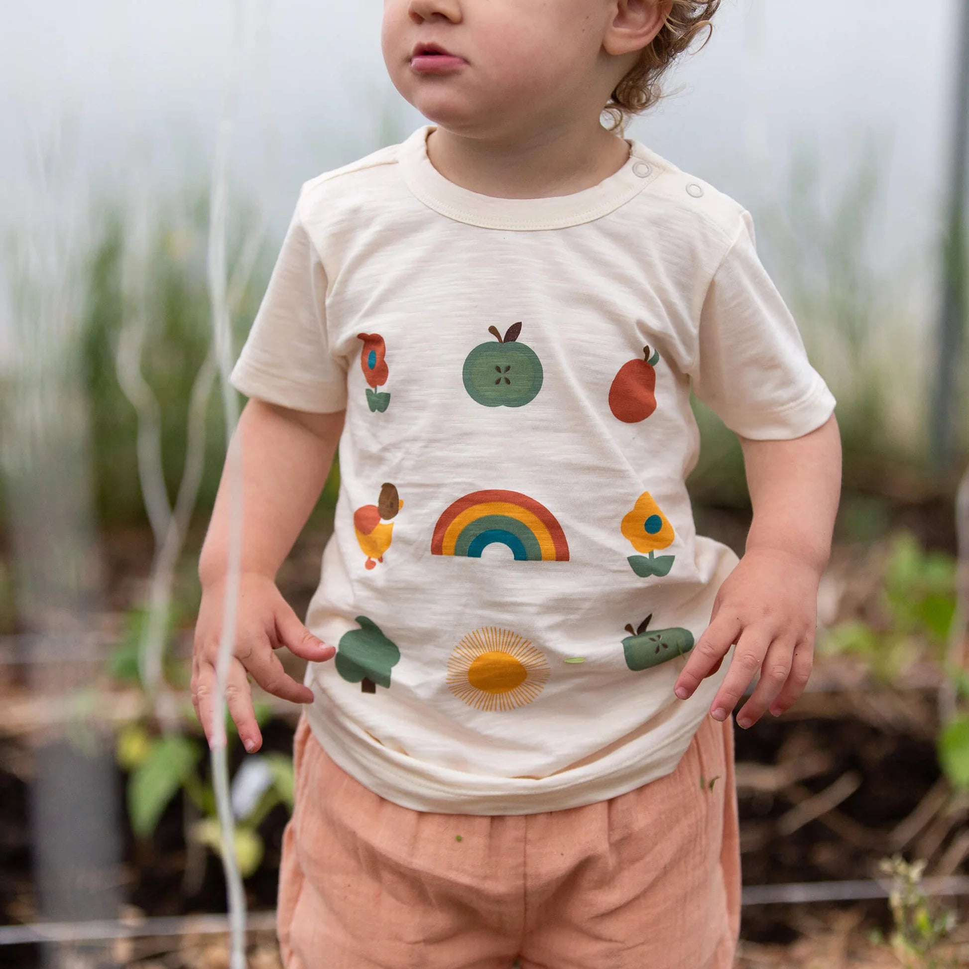 Child wearing a shirt with colorful nature-themed designs in an outdoor setting