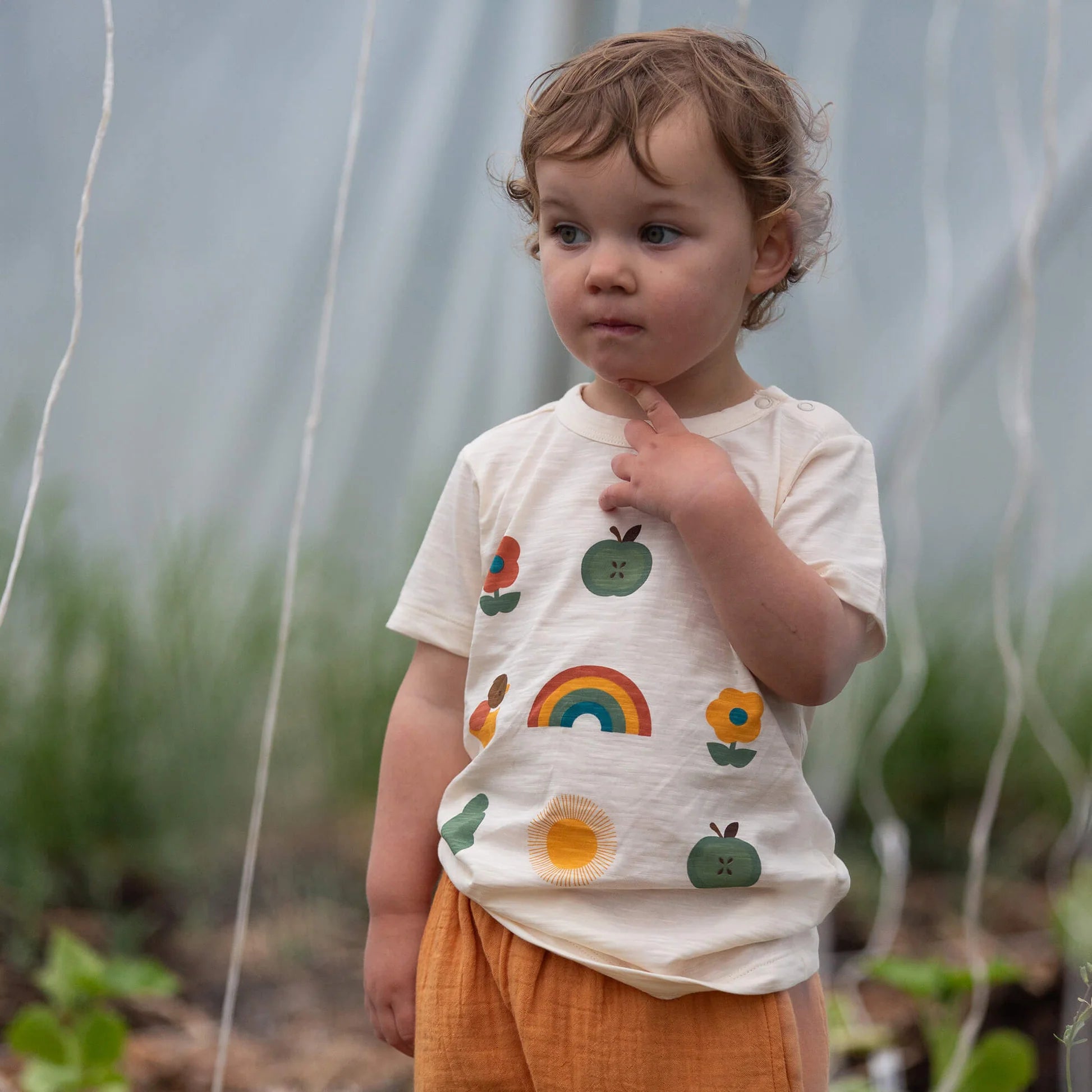 Child wearing a shirt with colorful patterns standing in a garden.
