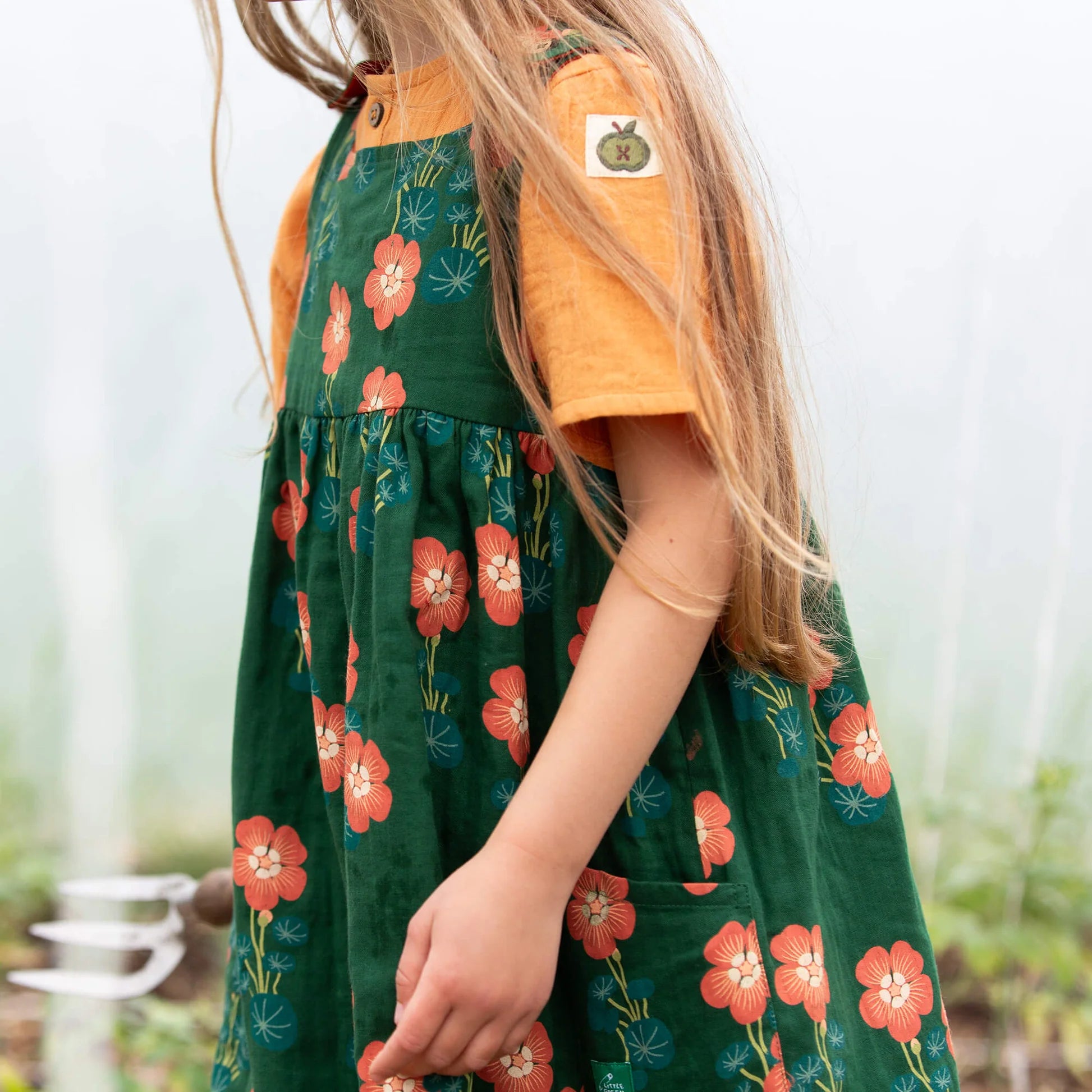 Person wearing a green floral dress with an orange shirt, standing in a garden.