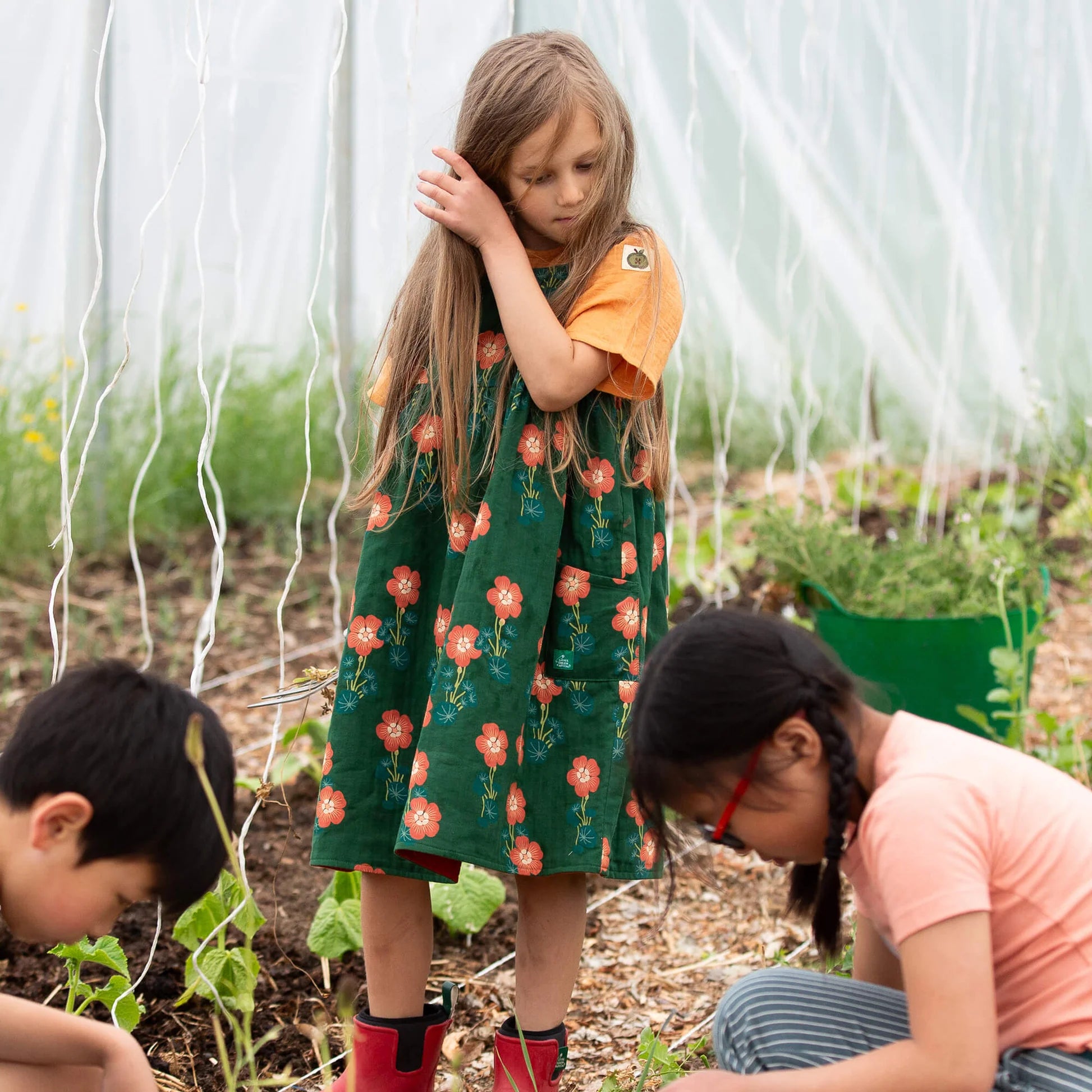 Children in a garden, with a focus on a girl in a floral dress.