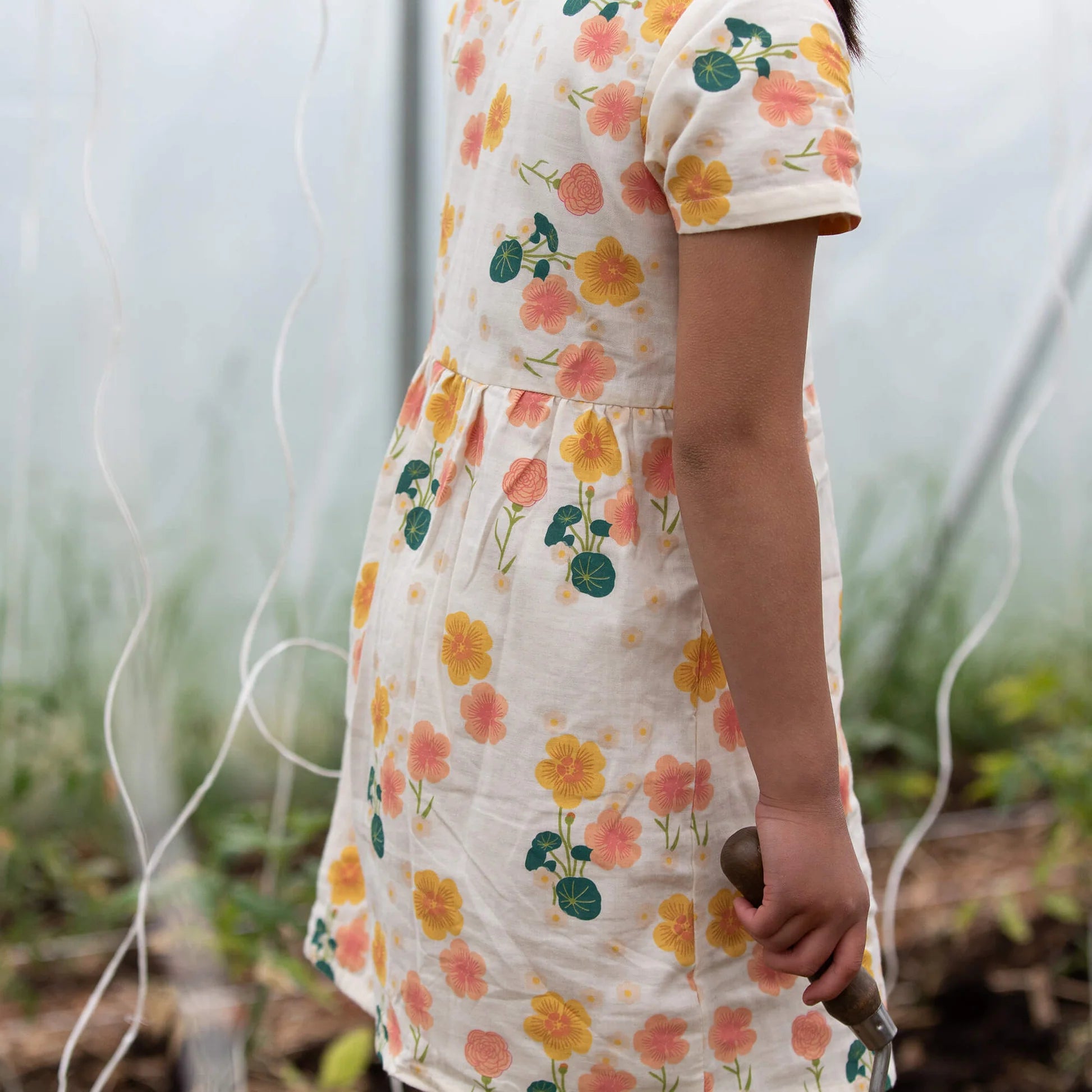 Person wearing a floral dress holding a garden tool in a garden setting