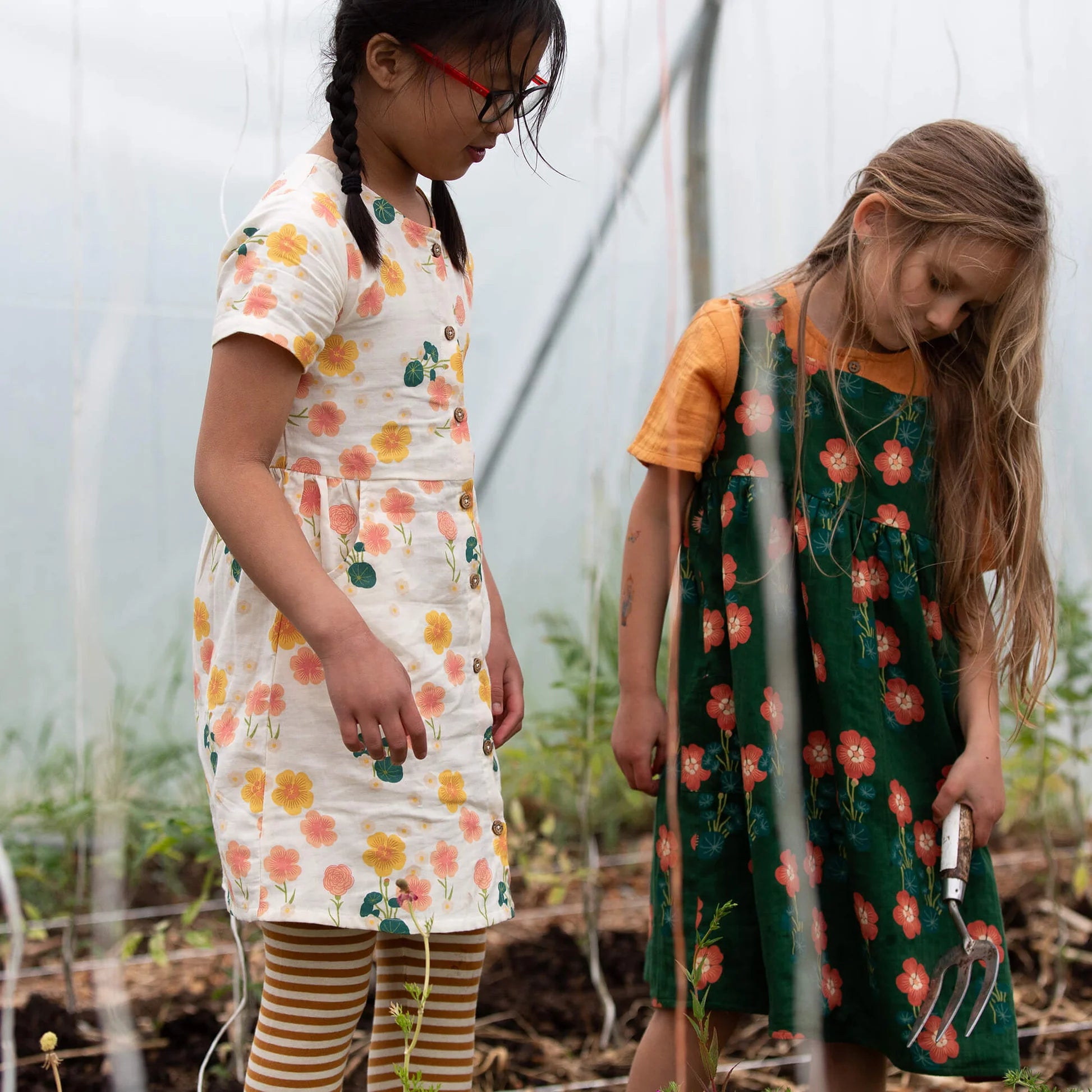 Two young girls in floral dresses standing in a garden.