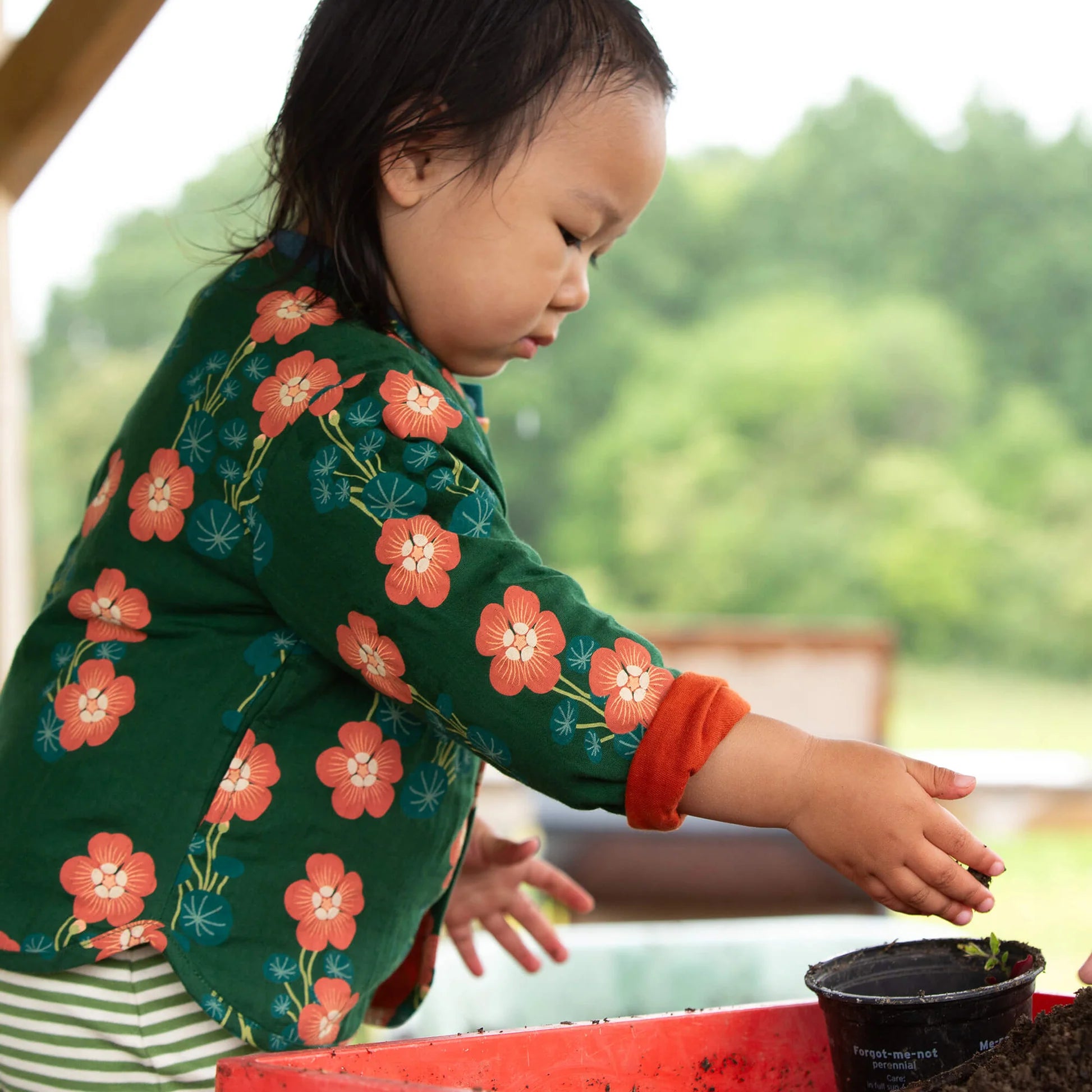 Child in a floral jacket interacting with a small black container outdoors