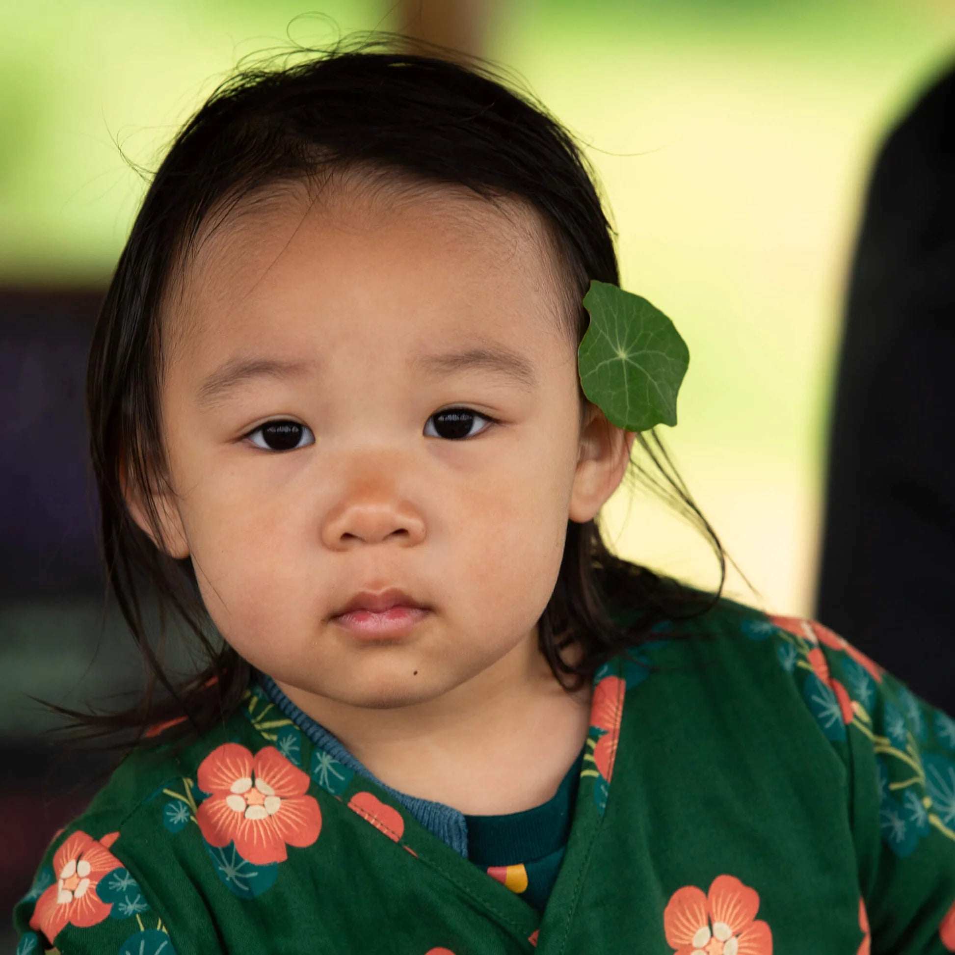 Child wearing a green floral outfit with a blurred background