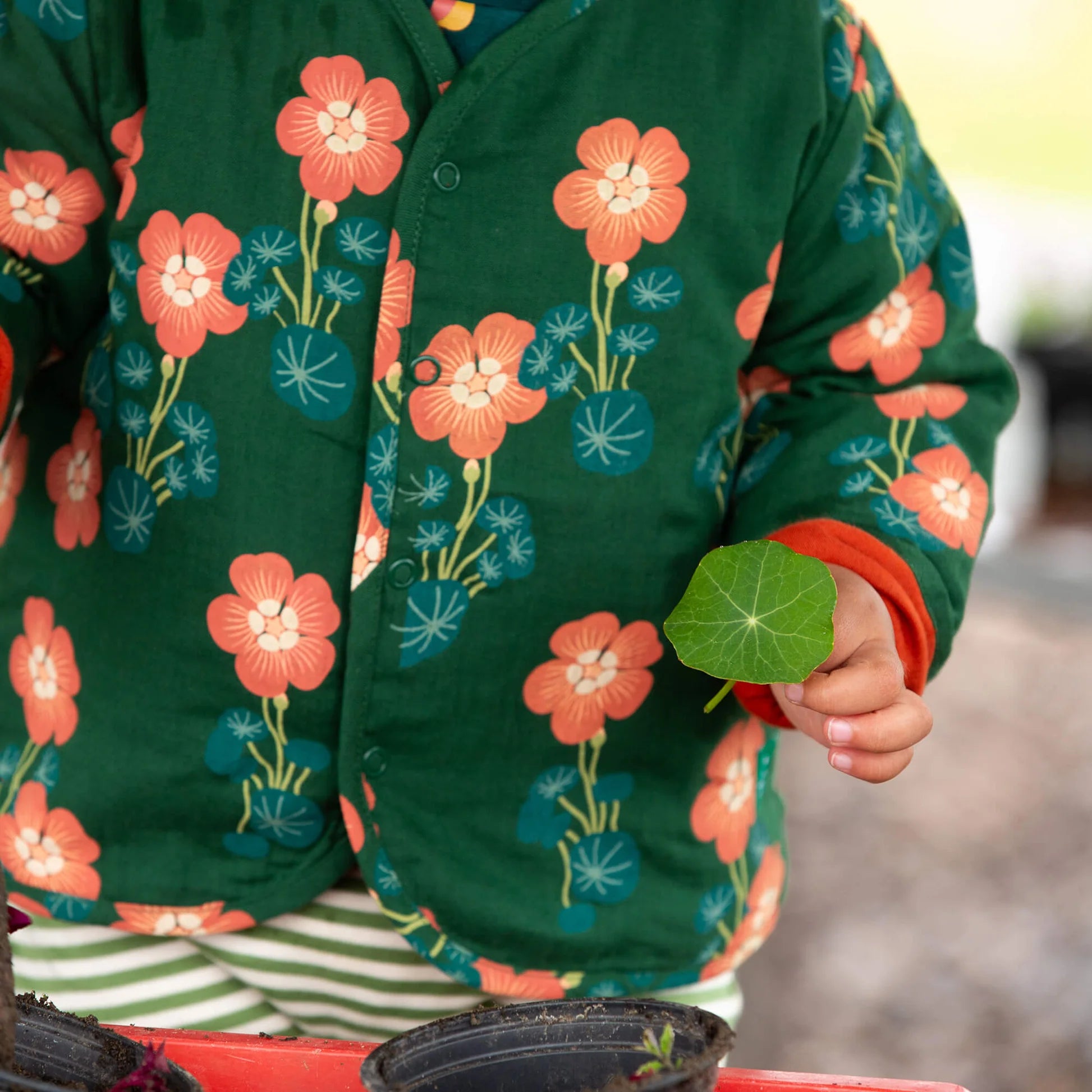 Person wearing a green jacket with floral patterns holding a green leaf.