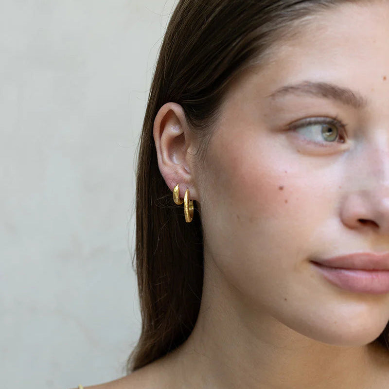 Close-up of a woman wearing gold hoop earrings against a neutral background