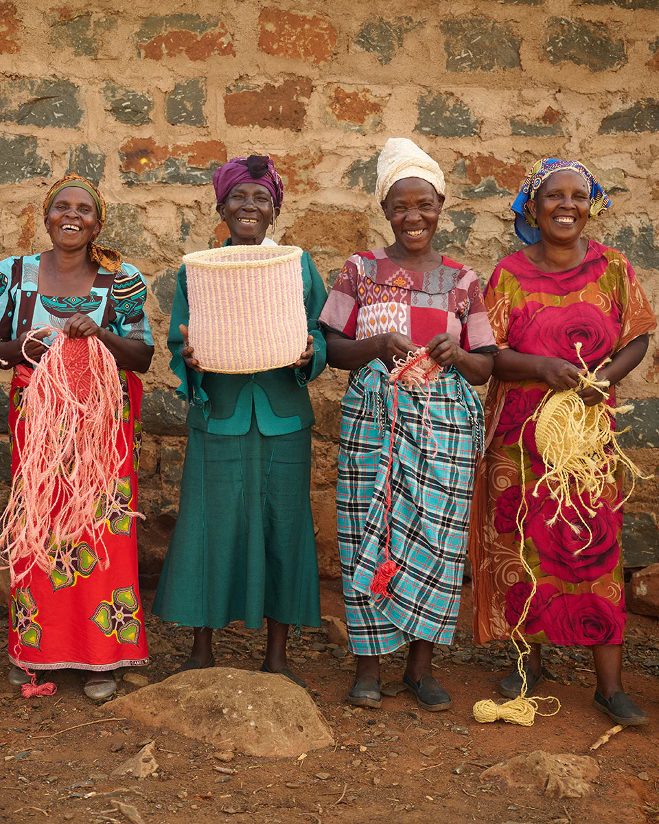 Pink and white striped woven basket held by a woman, surrounded by other women holding weaving materials.