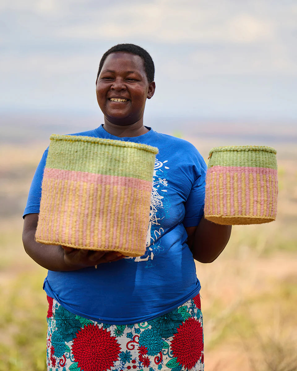 Two handcrafted woven baskets; light green, pink, and tan stripes; held by a woman.