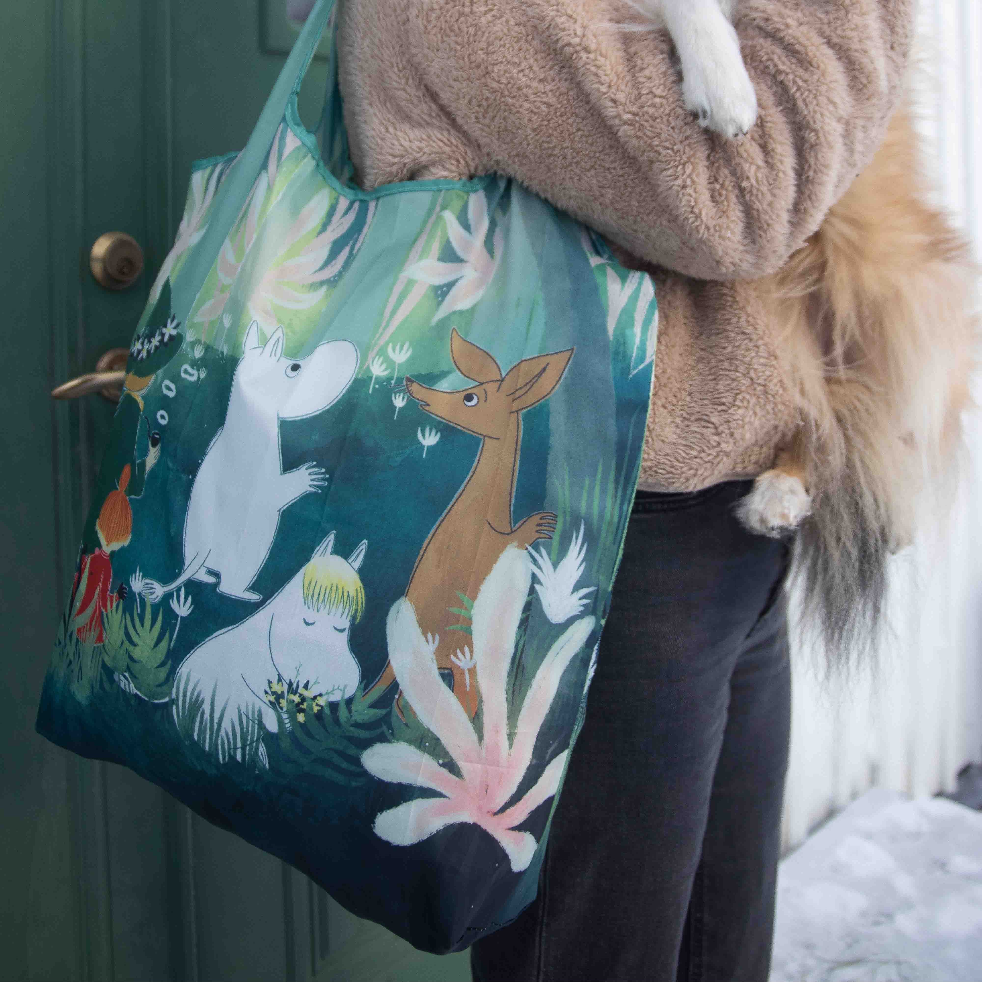 Person holding a dog and a tote bag with animal designs in front of a door.