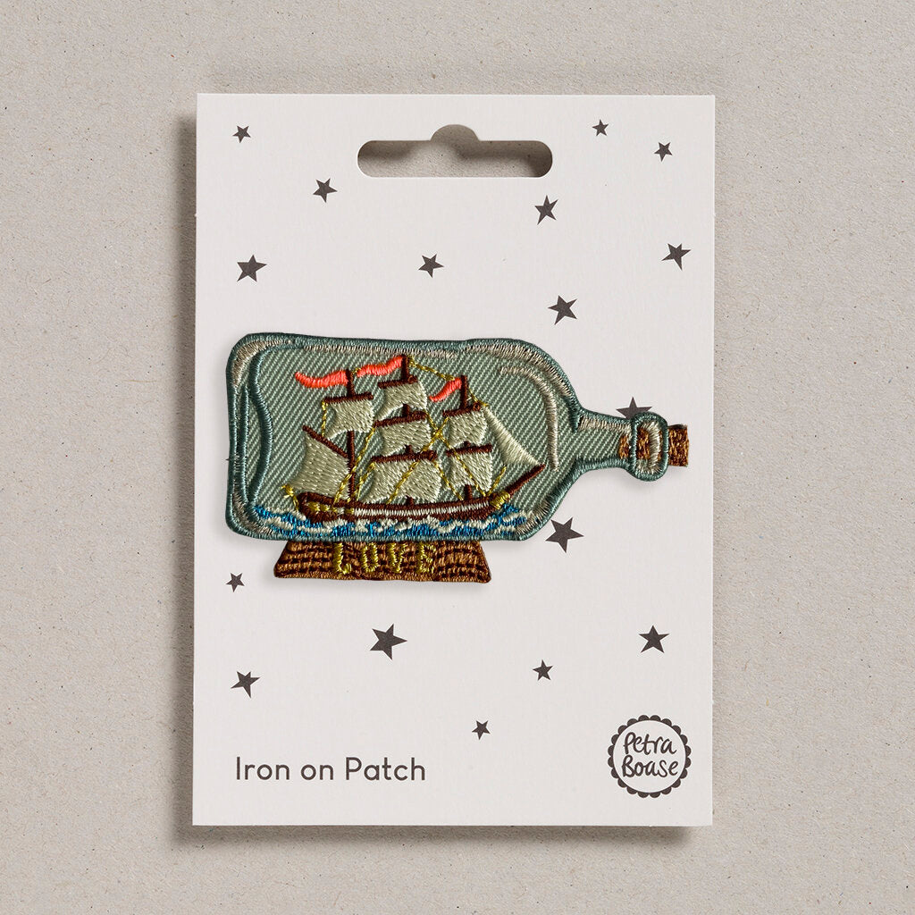 Embroidered iron-on patch depicting a sailing ship inside a glass bottle.