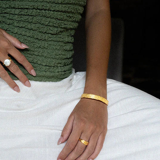Person wearing a green top and white pants with gold jewelry.