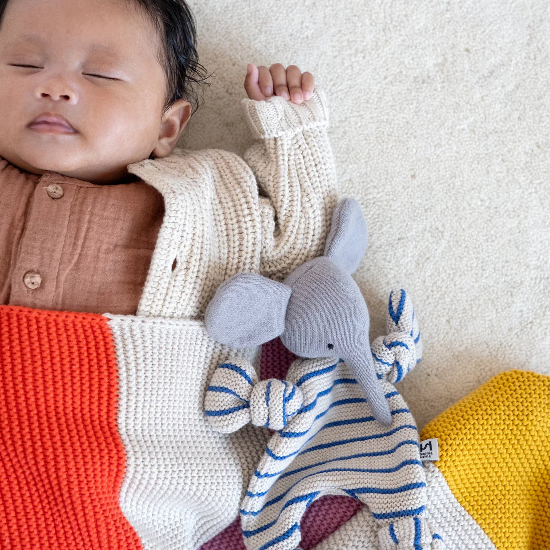 Baby sleeping with a striped toy on a textured surface