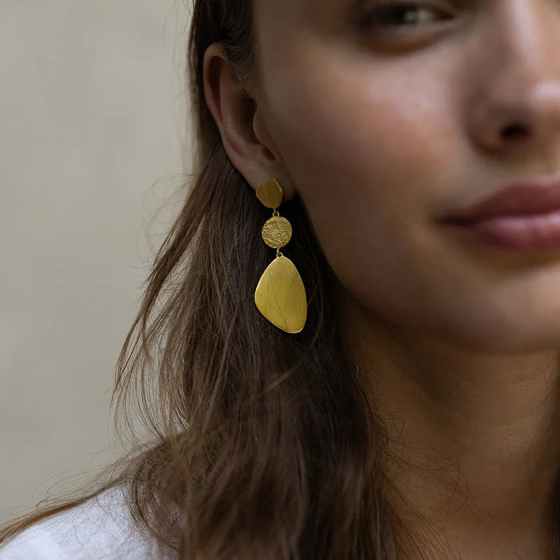 Close-up of a person wearing gold earrings with a neutral background