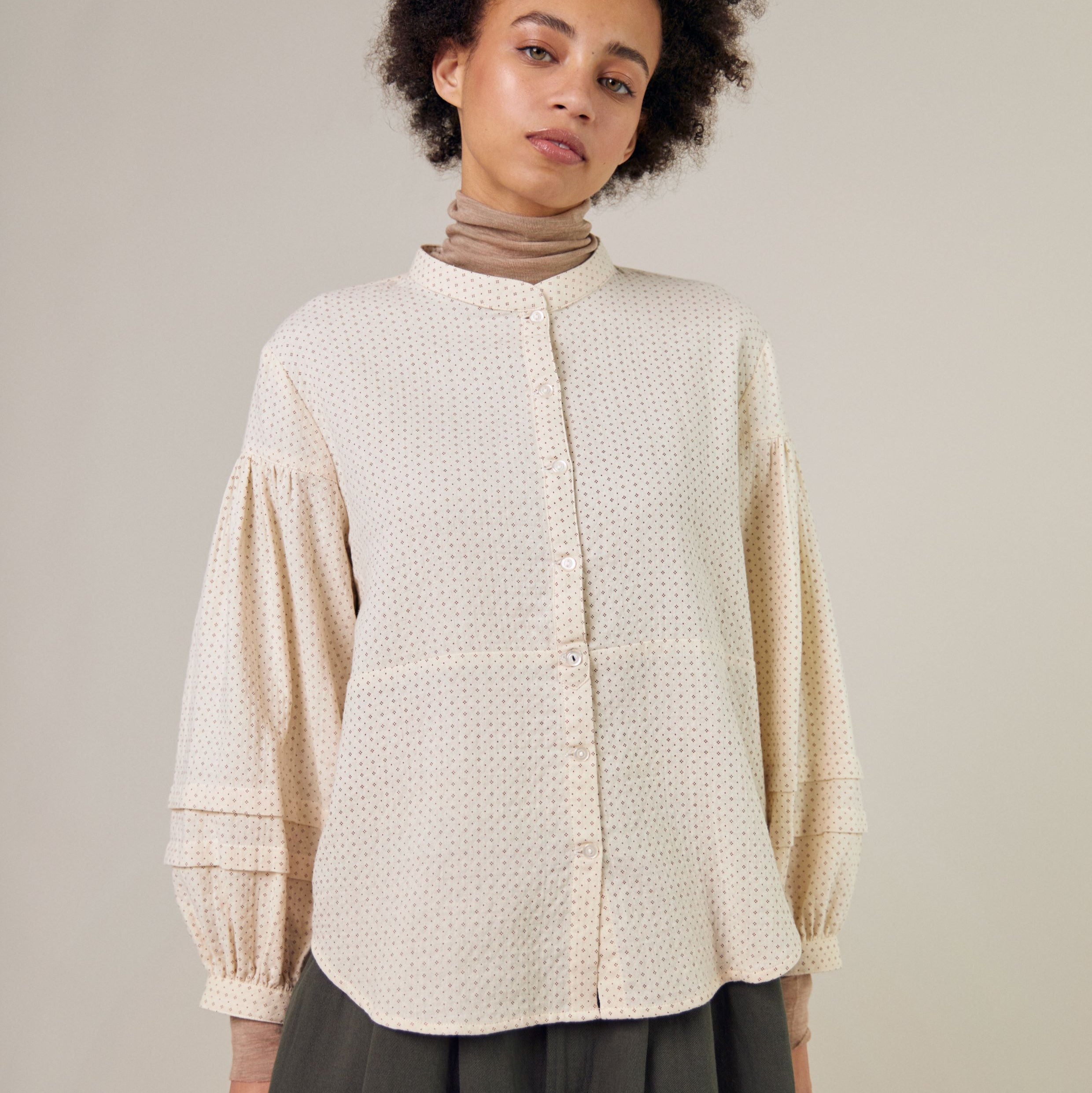 Cream-colored button-down shirt with a subtle brown dot pattern, featuring long balloon sleeves and a mandarin collar.