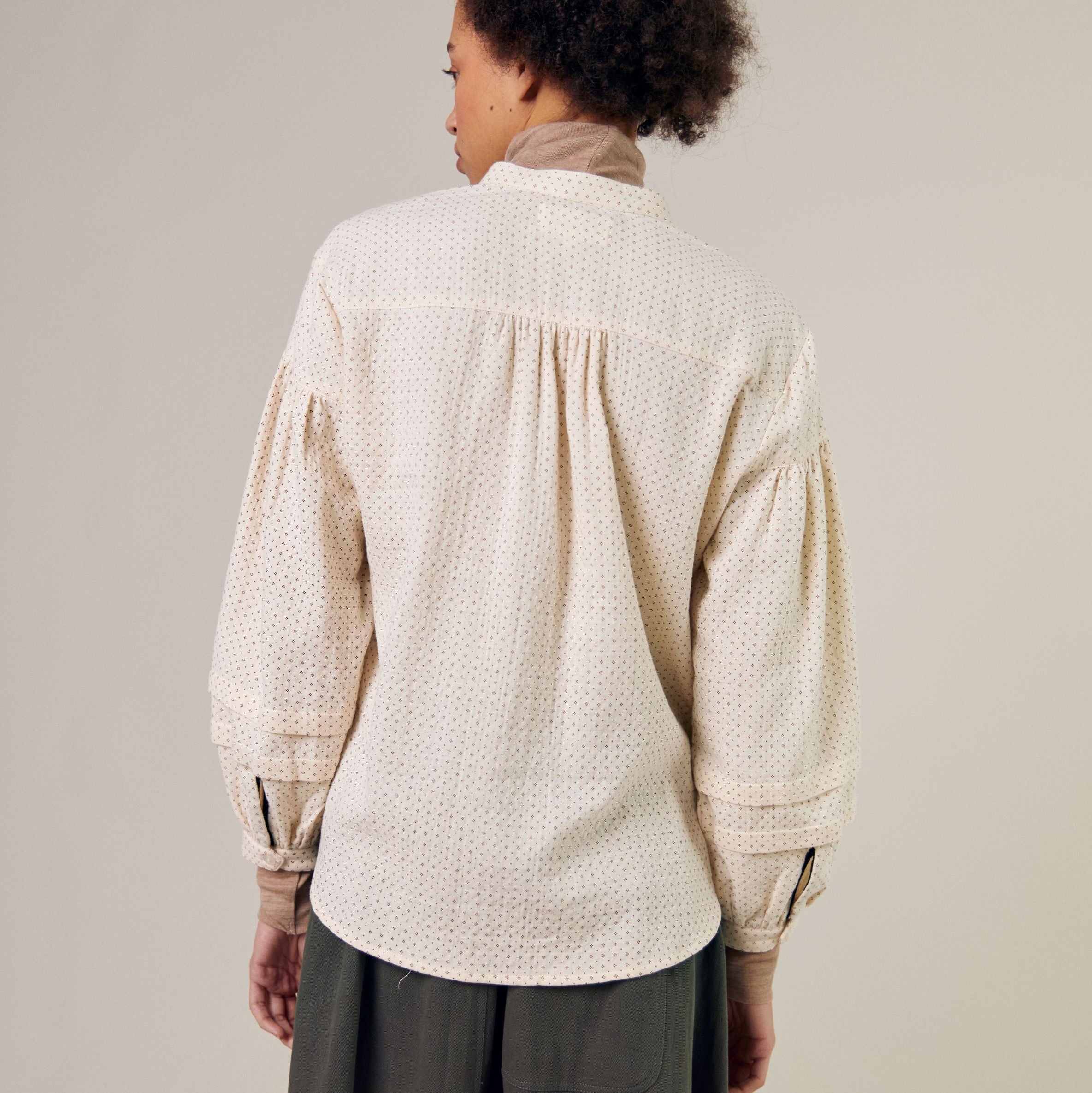 Cream-colored, long-sleeve button-down shirt with a subtle dotted pattern and slightly puffed sleeves.