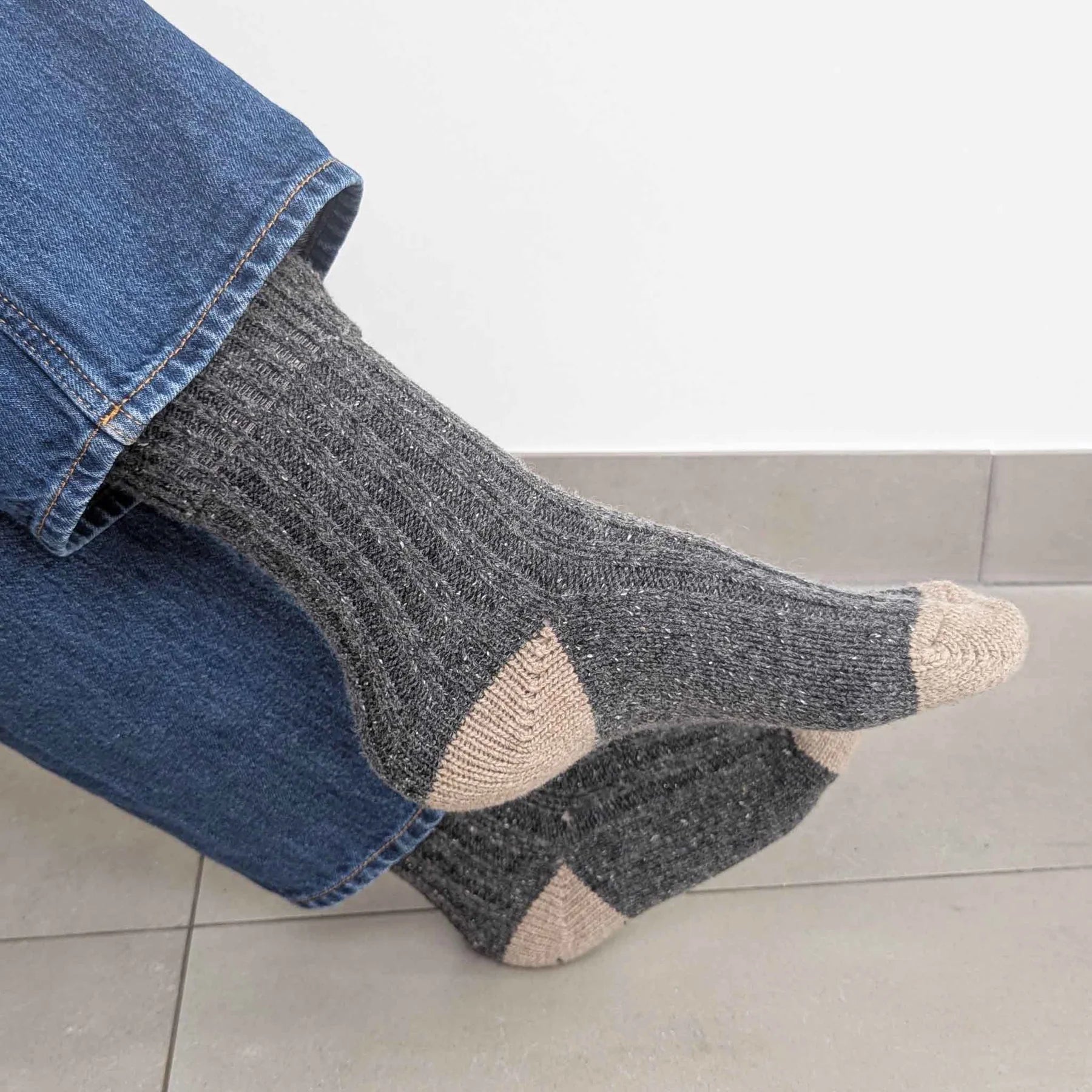 Gray socks with beige accents worn with blue jeans on a light gray floor.