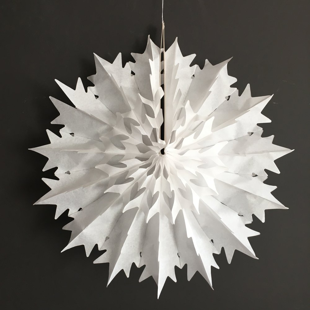 Large white paper snowflake decoration with a pointed, starburst design. It's hanging from a thin string.