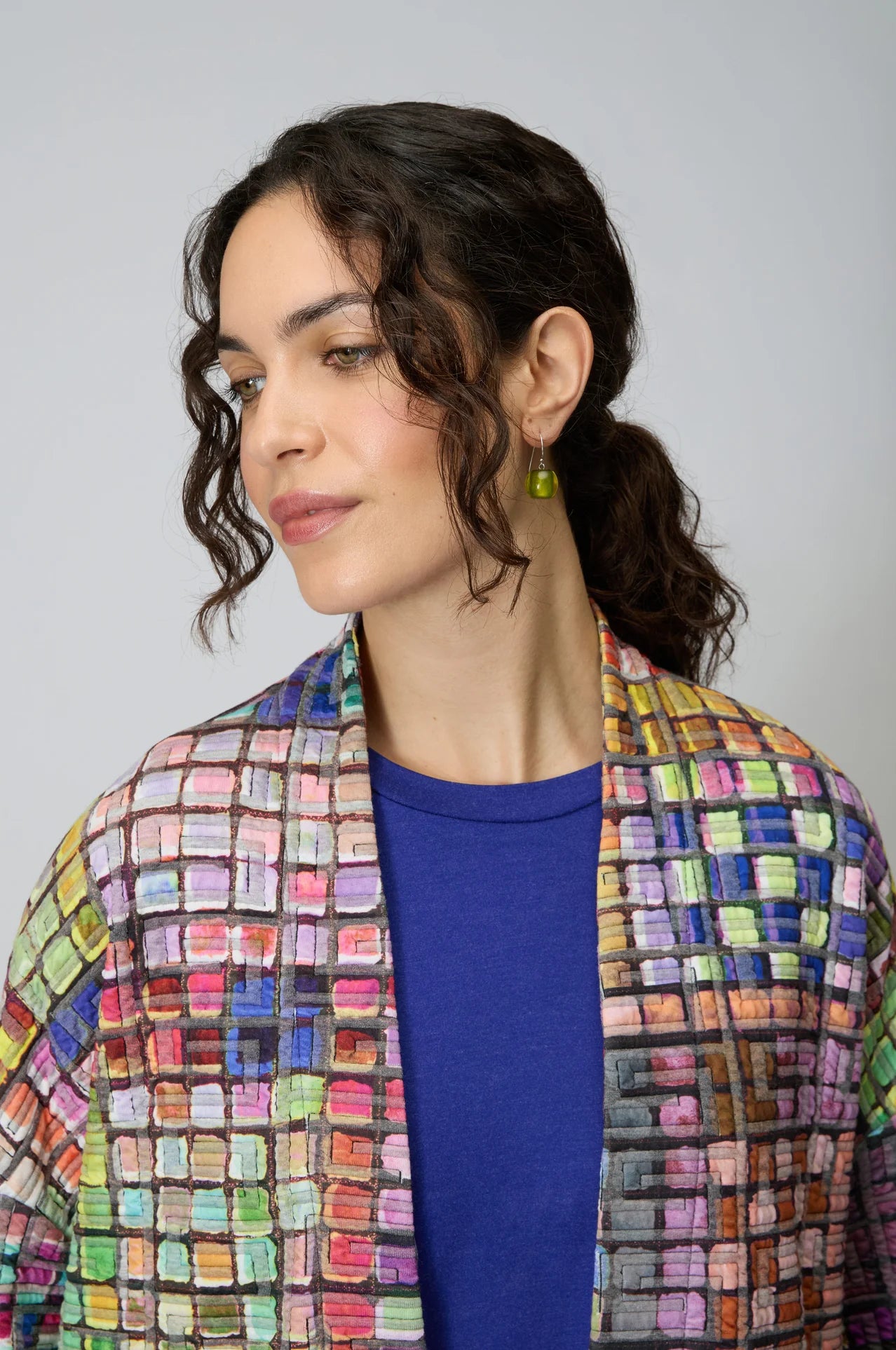 Woman wearing a colorful checkered jacket over a blue top against a gray background