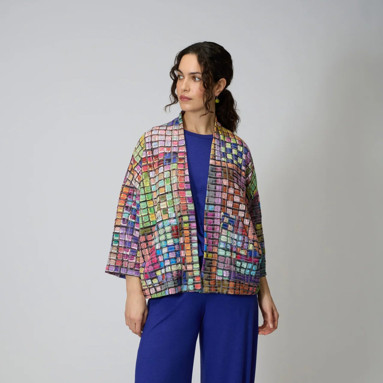 Woman wearing a colorful quilted jacket and blue pants on a white background