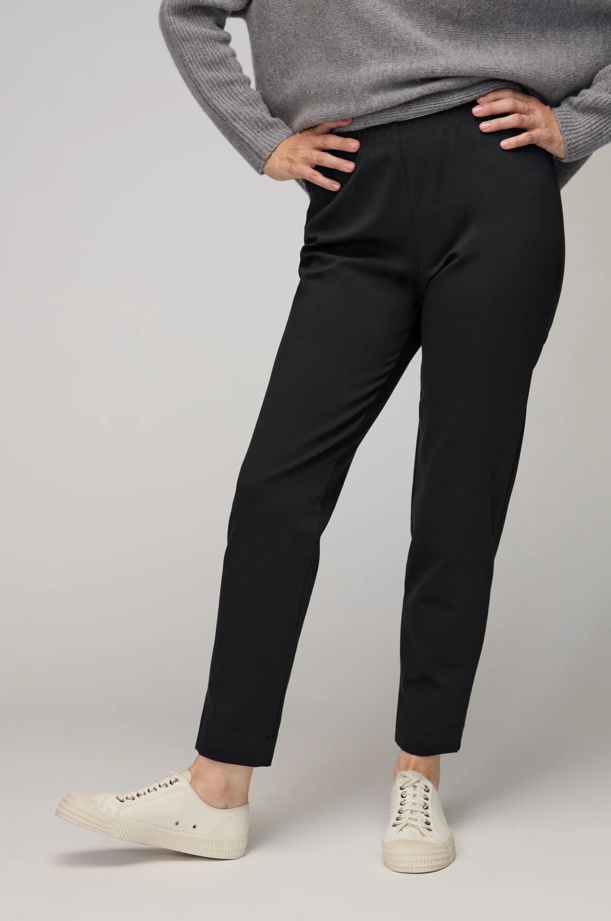 Person wearing black pants and a gray sweater on a plain background