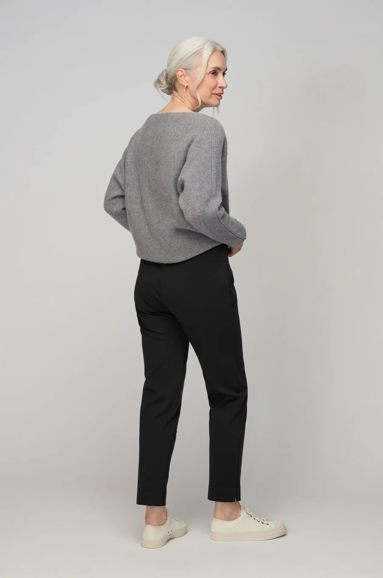 Person wearing a gray sweater and black pants on a plain background