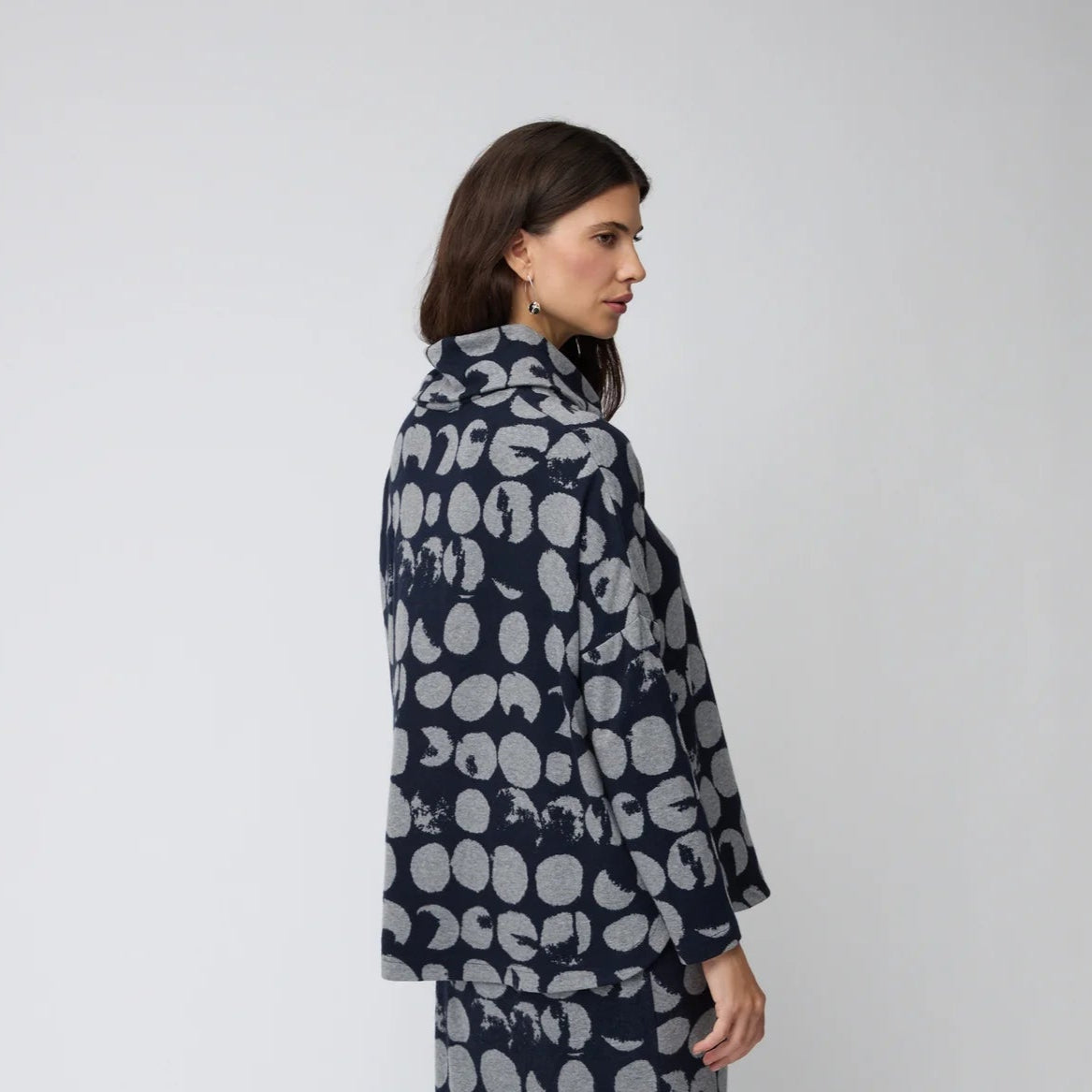 Woman wearing a navy coat with white pattern on a plain background