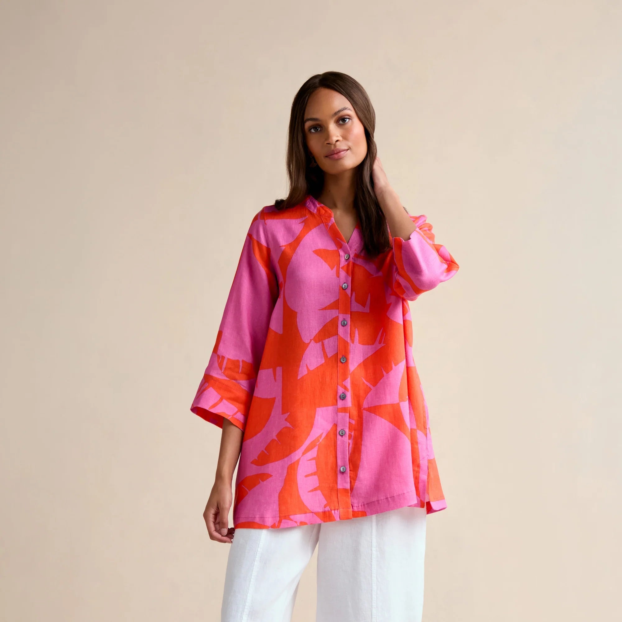 Woman wearing a pink and orange patterned shirt with white pants on a beige background