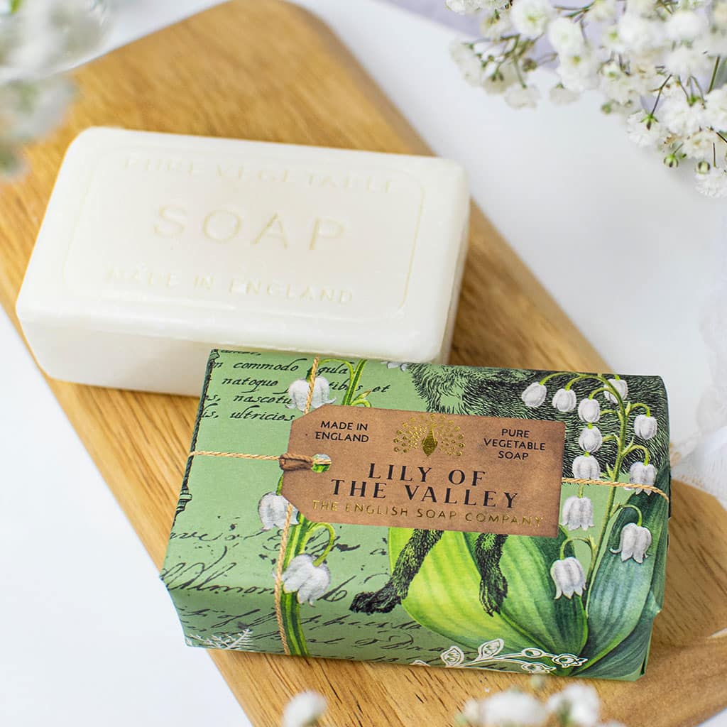 Two bars of soap; one plain white bar, the other wrapped in green paper with a lily of the valley design and "Lily of the