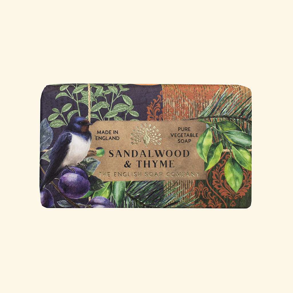 A rectangular bar of soap in a decorative paper wrapper featuring a swallow bird, green leaves, purple berries, and a wood-grain texture. The central label reads 'SANDALWOOD & THYME' and 'THE ENGLISH SOAP COMPANY'.