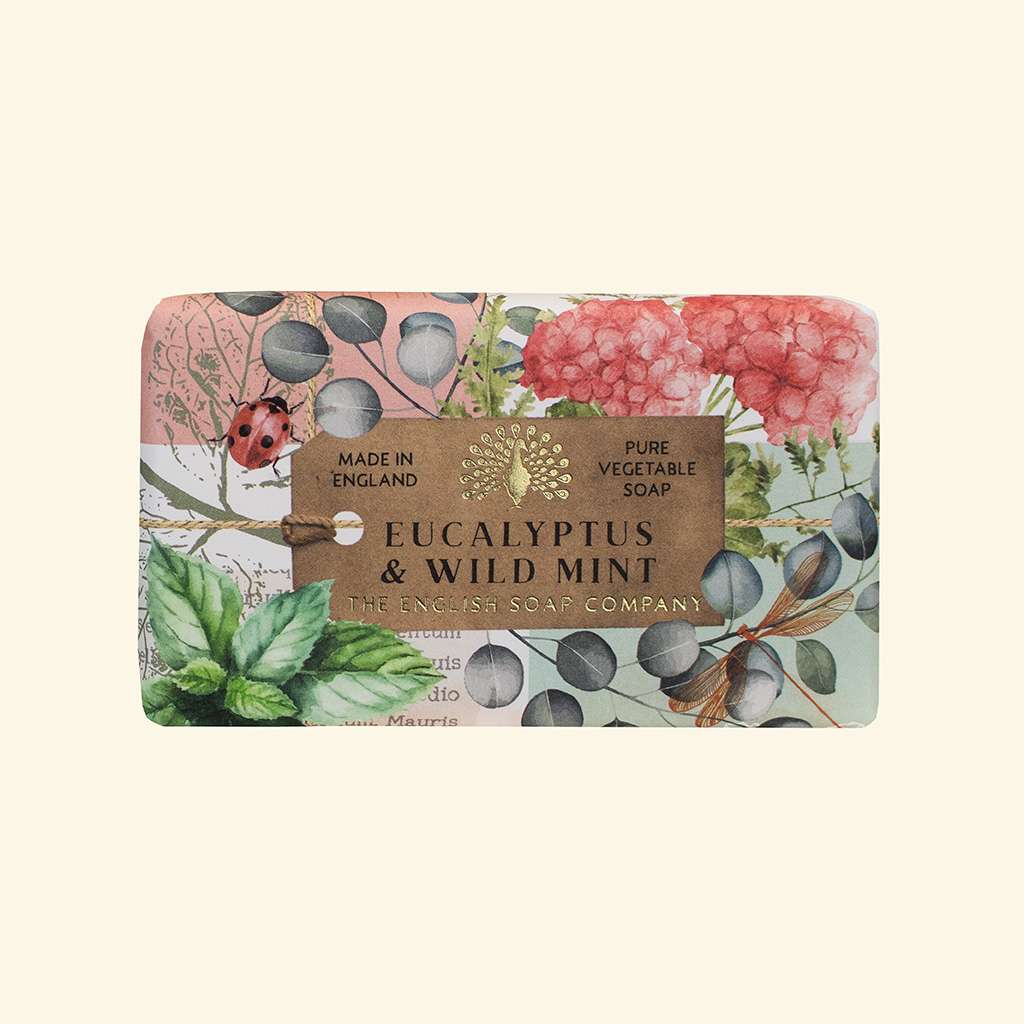 A rectangular bar of soap wrapped in a botanical paper sleeve, featuring pink hydrangeas, green leaves, blue berries, and a ladybug illustration. A brown paper band across the front reads 'EUCALYPTUS & WILD MINT' and 'THE ENGLAND SOAP COMPANY'.