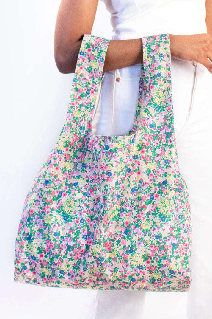 Reusable shopping tote bag with a small-scale floral print in pink, purple, green, and yellow on a cream background.