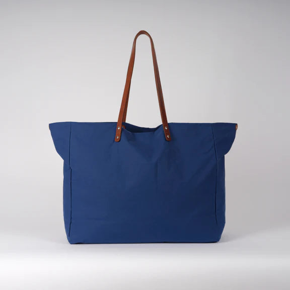 Large cobalt blue tote bag with brown leather handles and silver-toned hardware.
