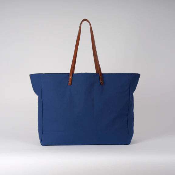 Large cobalt blue tote bag with brown leather handles.