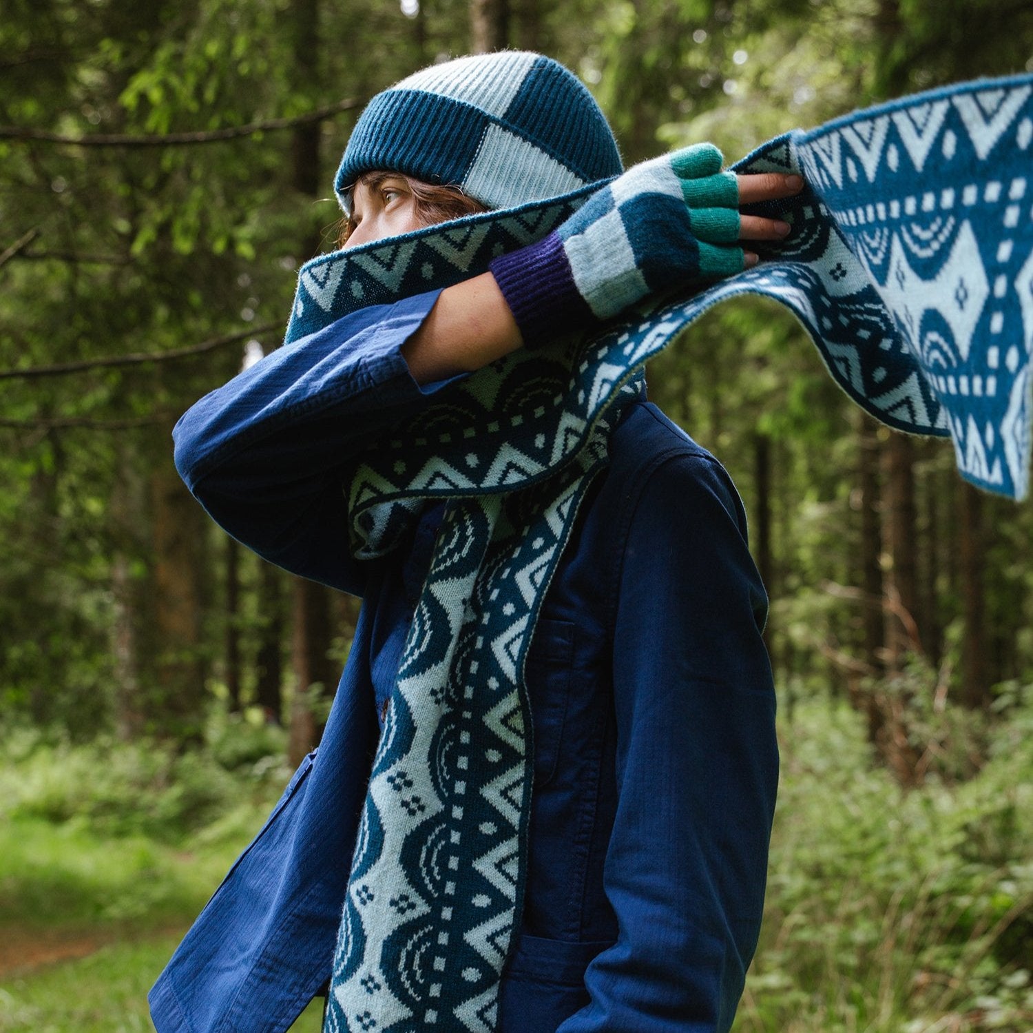 Blue and teal patterned knit scarf and matching gloves, with a blue and white checked knit hat.