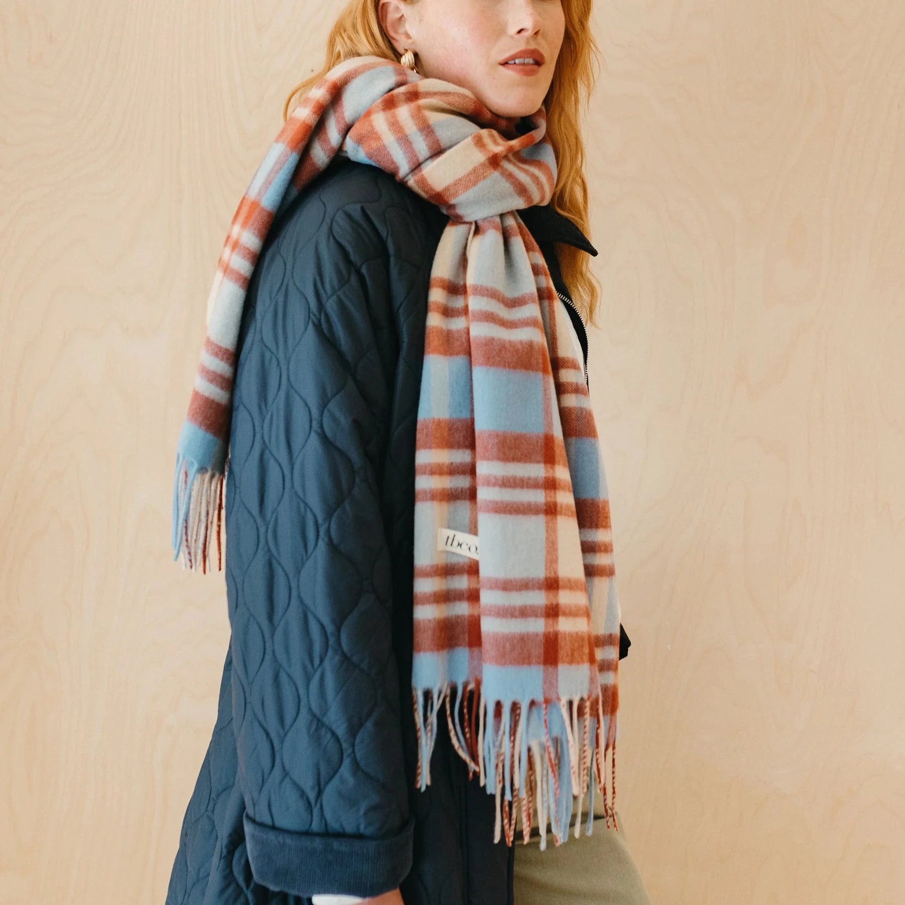 Soft, fringed plaid scarf in light blue, cream, and rust tones.