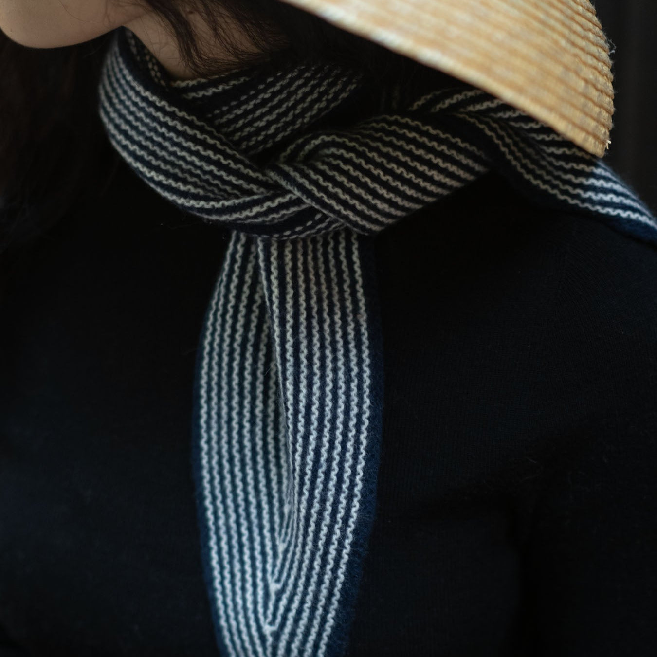A navy rib-knitted pure cashmere neck scarf with a striped pattern, worn around the neck.
