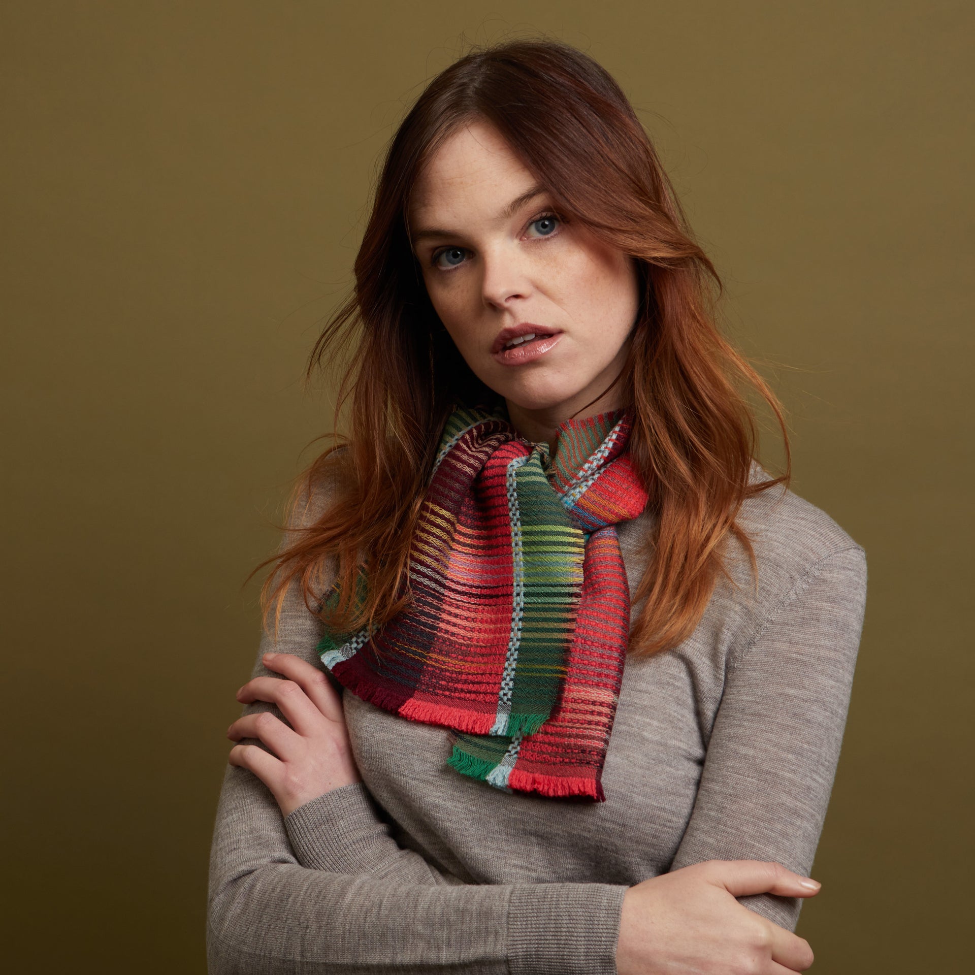 Multicolored woven scarf with red, green, and teal stripes, tied in a loose knot around the neck.
