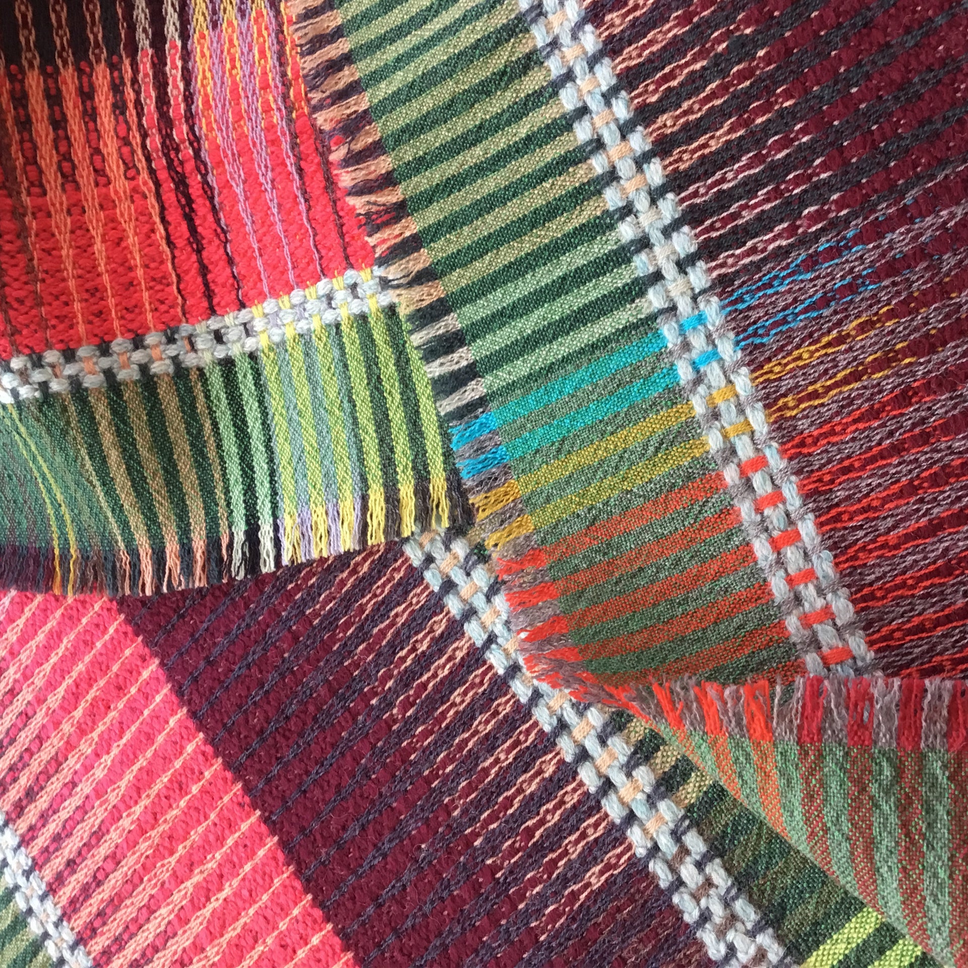 Close-up of a multicolored woven textile with a patchwork design featuring red, green, and brown stripes.
