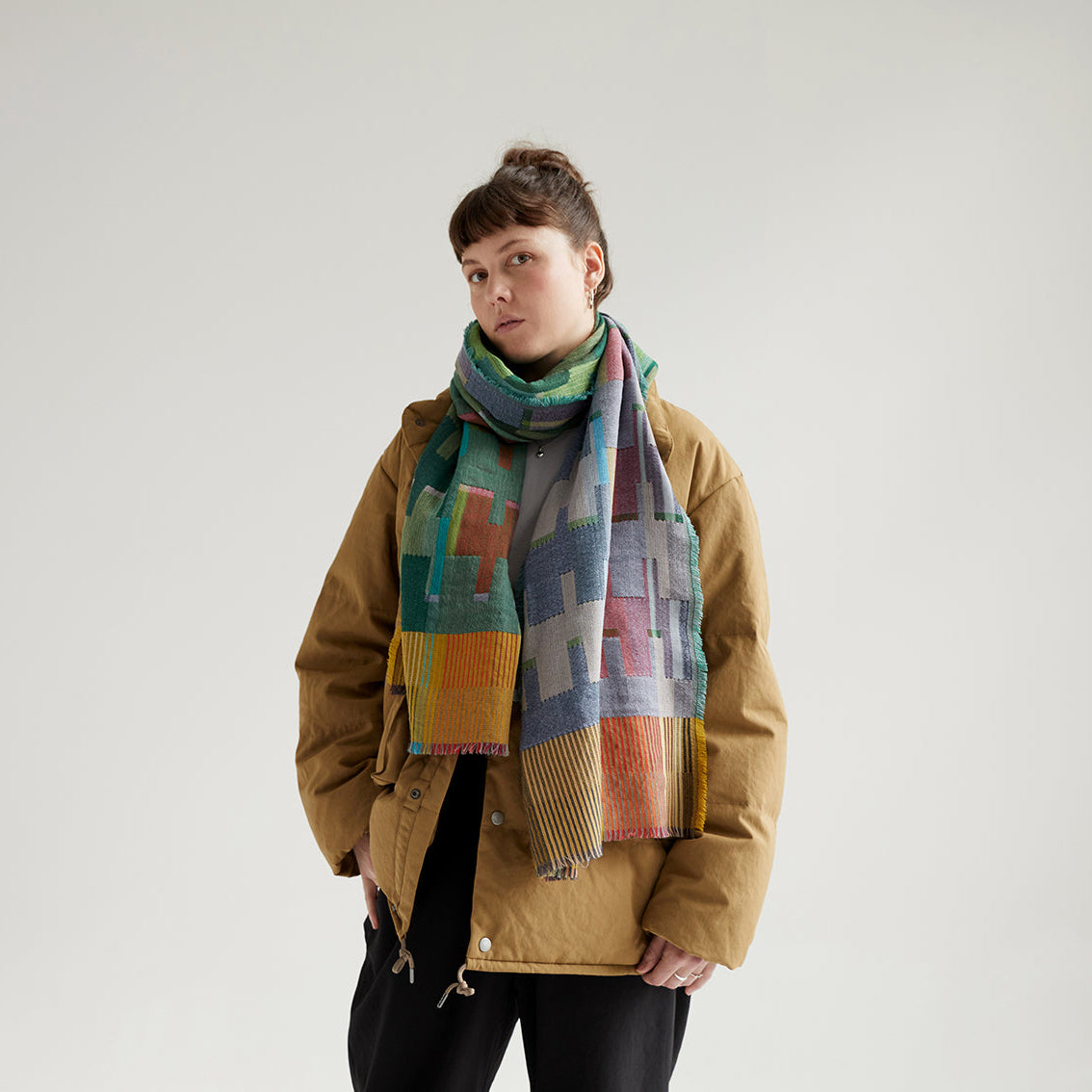 Woven scarf with a geometric pattern in teal, grey, orange, and yellow.  The scarf has a fringed edge.