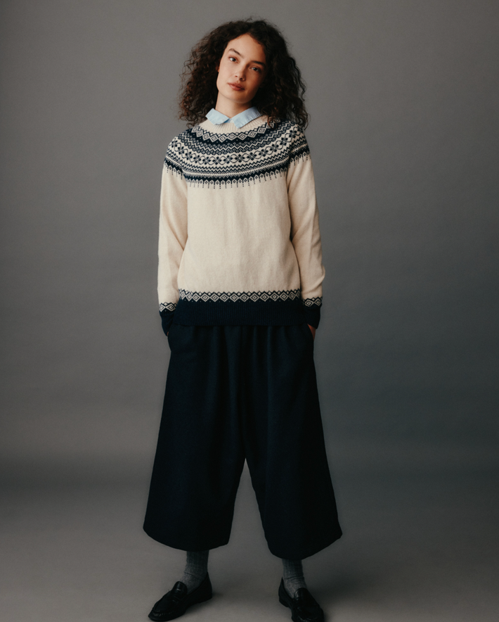 Woman wearing a cream sweater with a patterned neckline against a gray background
