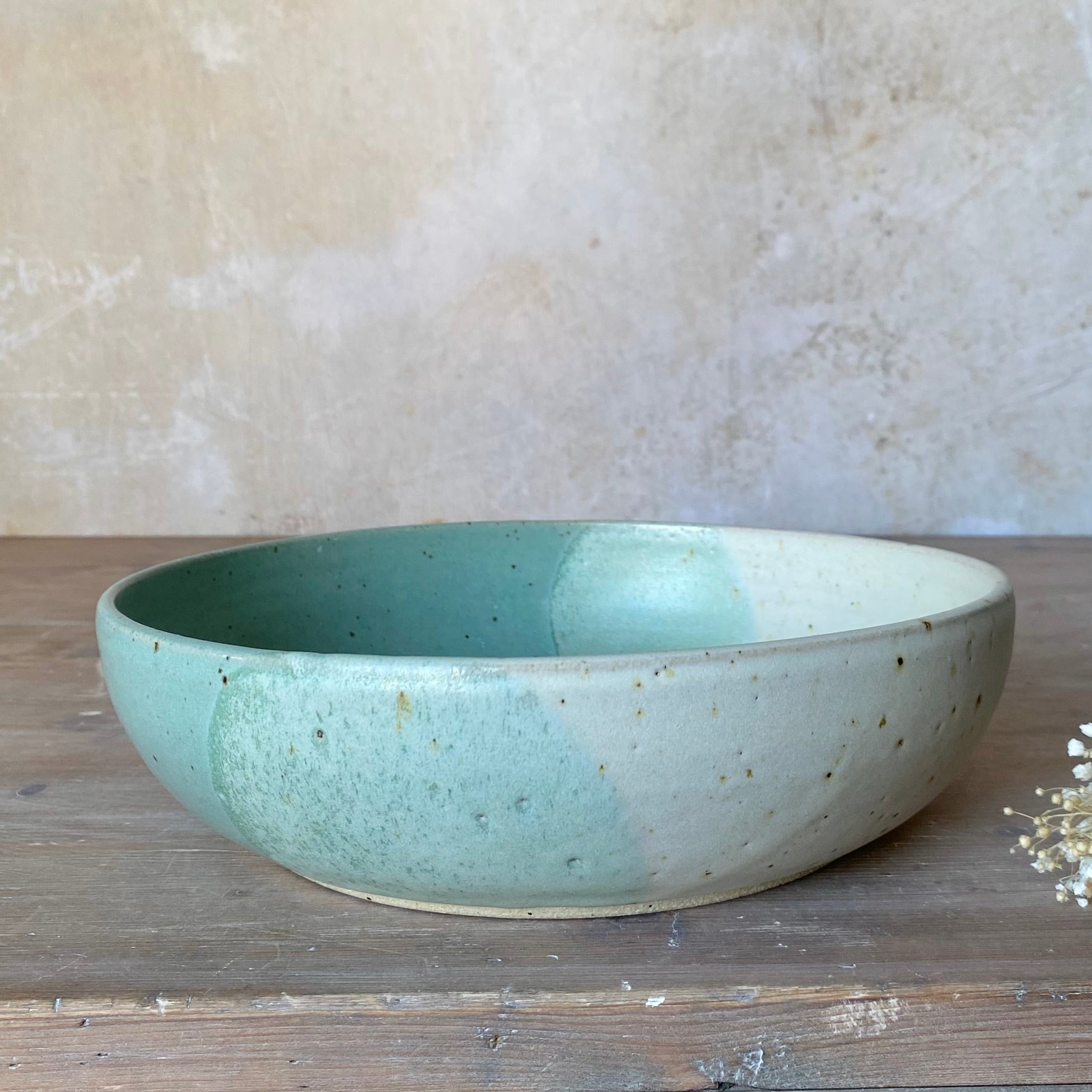 Large ceramic bowl with speckled, two-toned glaze in shades of seafoam green and off-white.