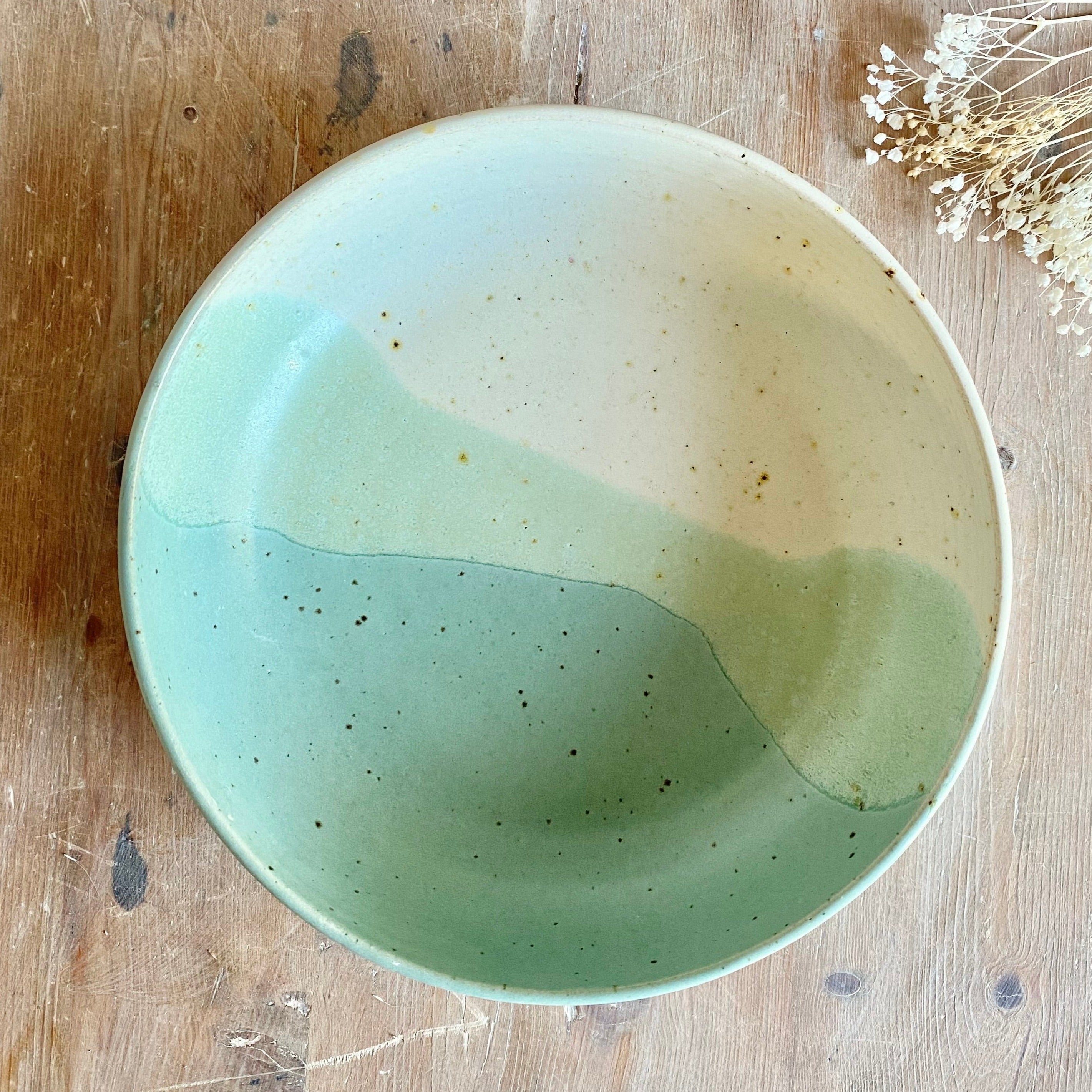 Large ceramic bowl with a speckled, two-toned glaze in shades of pale green and off-white.