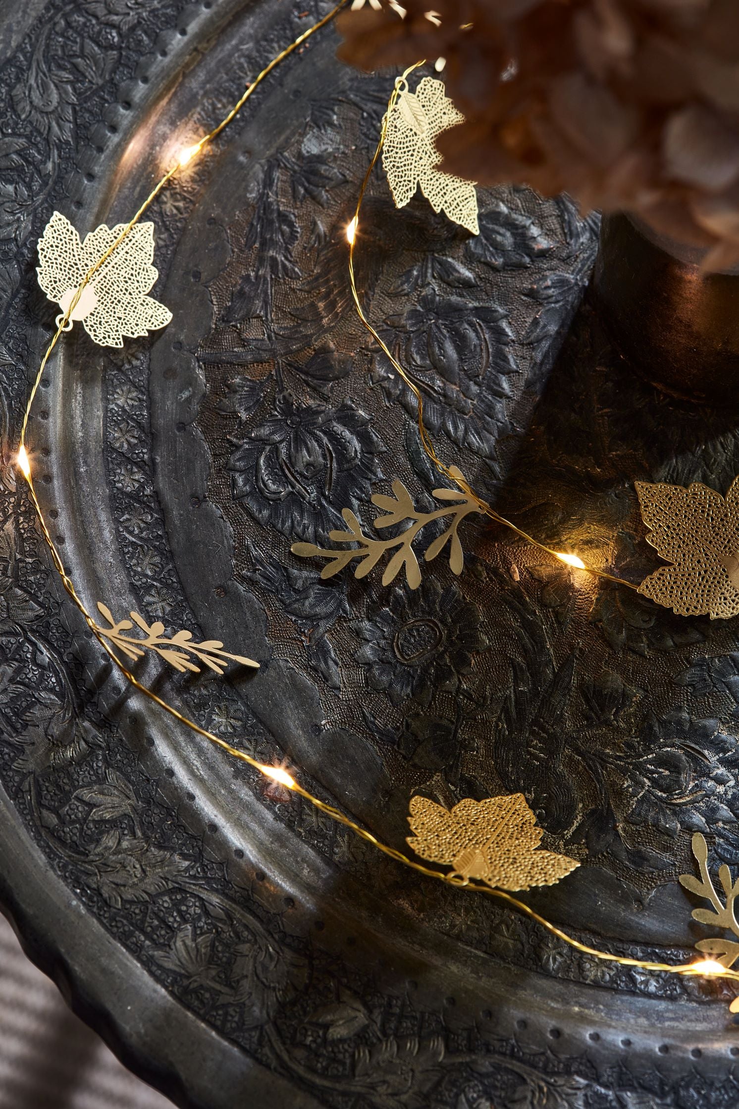 Gold leaf-shaped and sprig LED string lights draped on a dark, ornate surface.