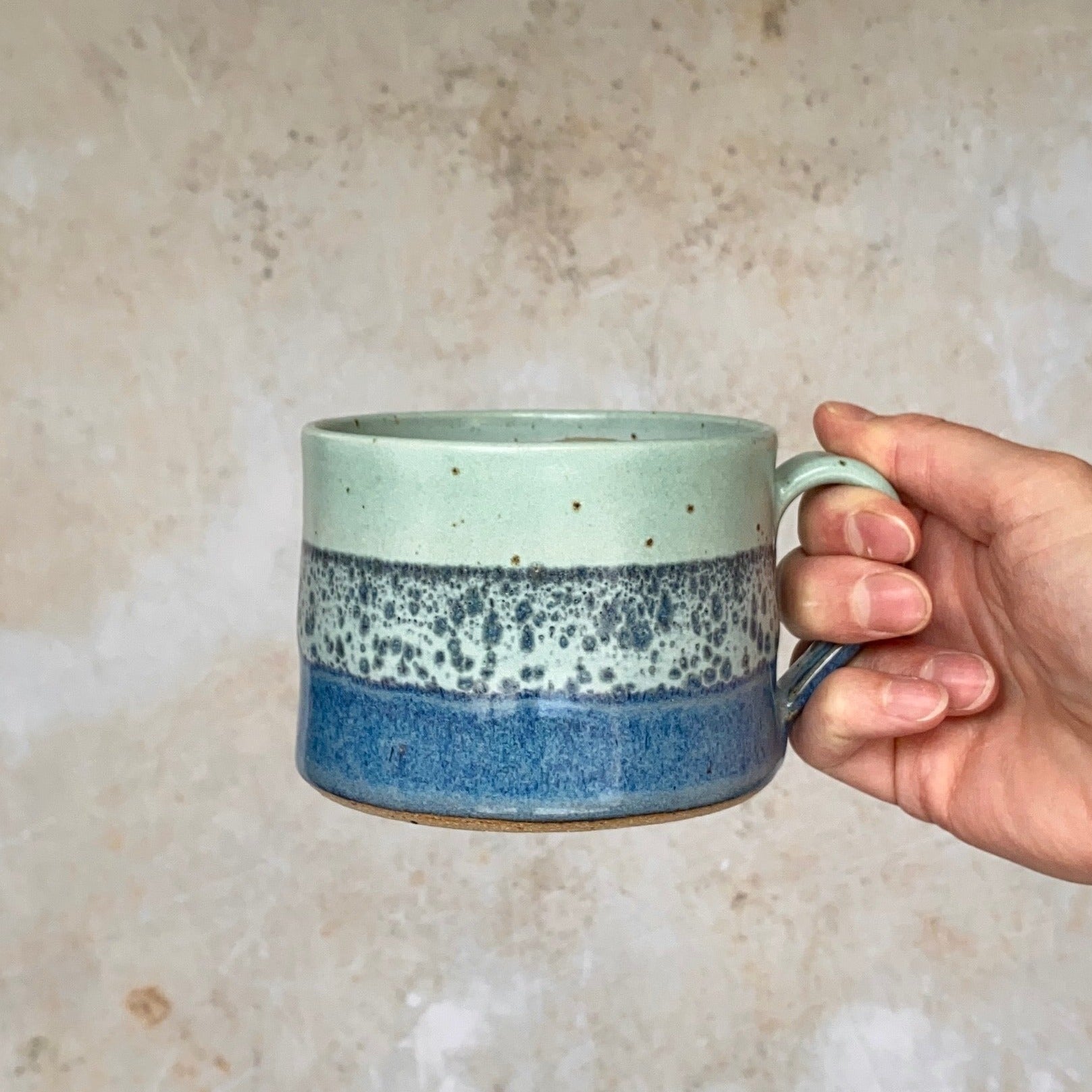 Hand holding a speckled blue and green ceramic mug.