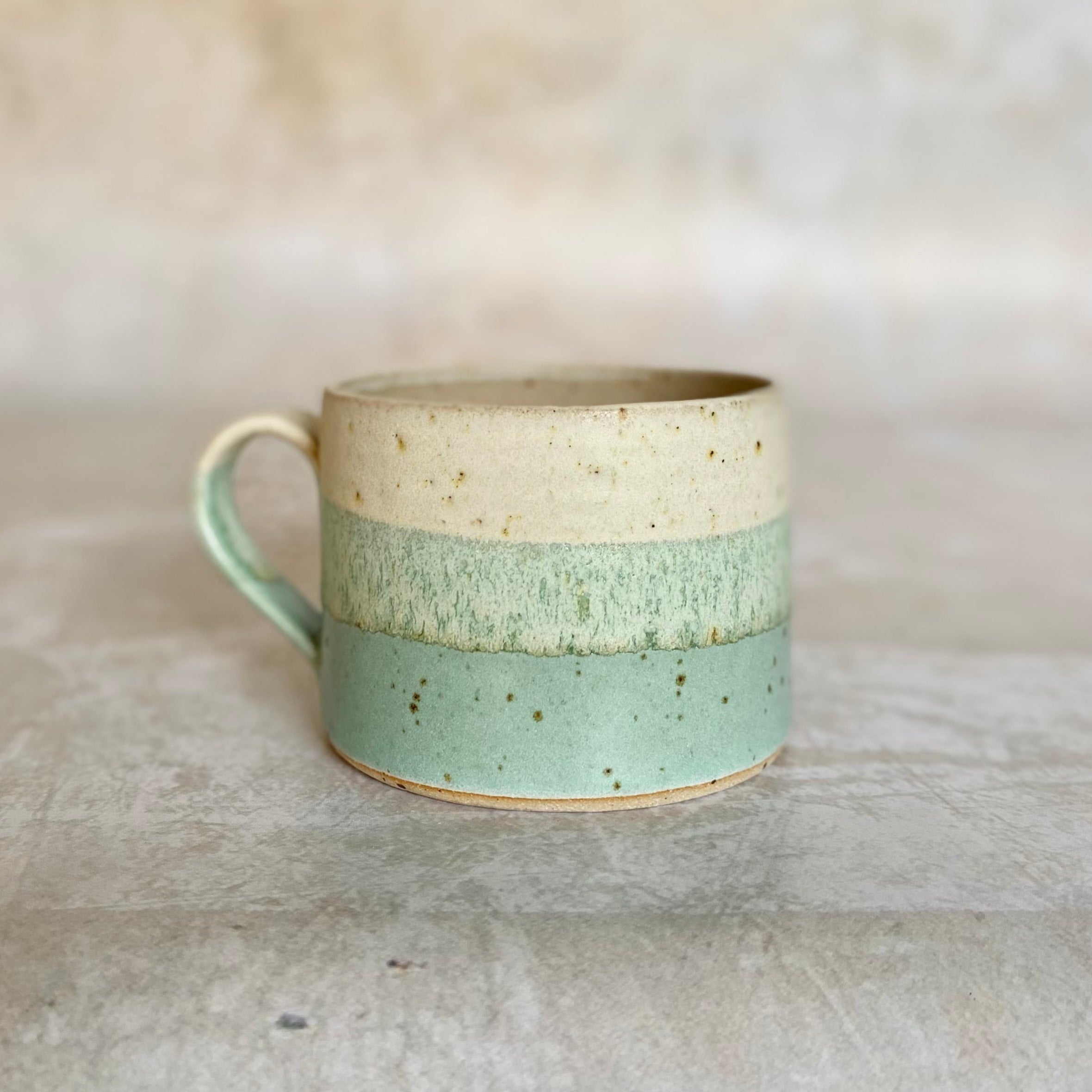 Hand-thrown stoneware mug with three horizontal bands of off-white, light green, and speckled seafoam green glaze.