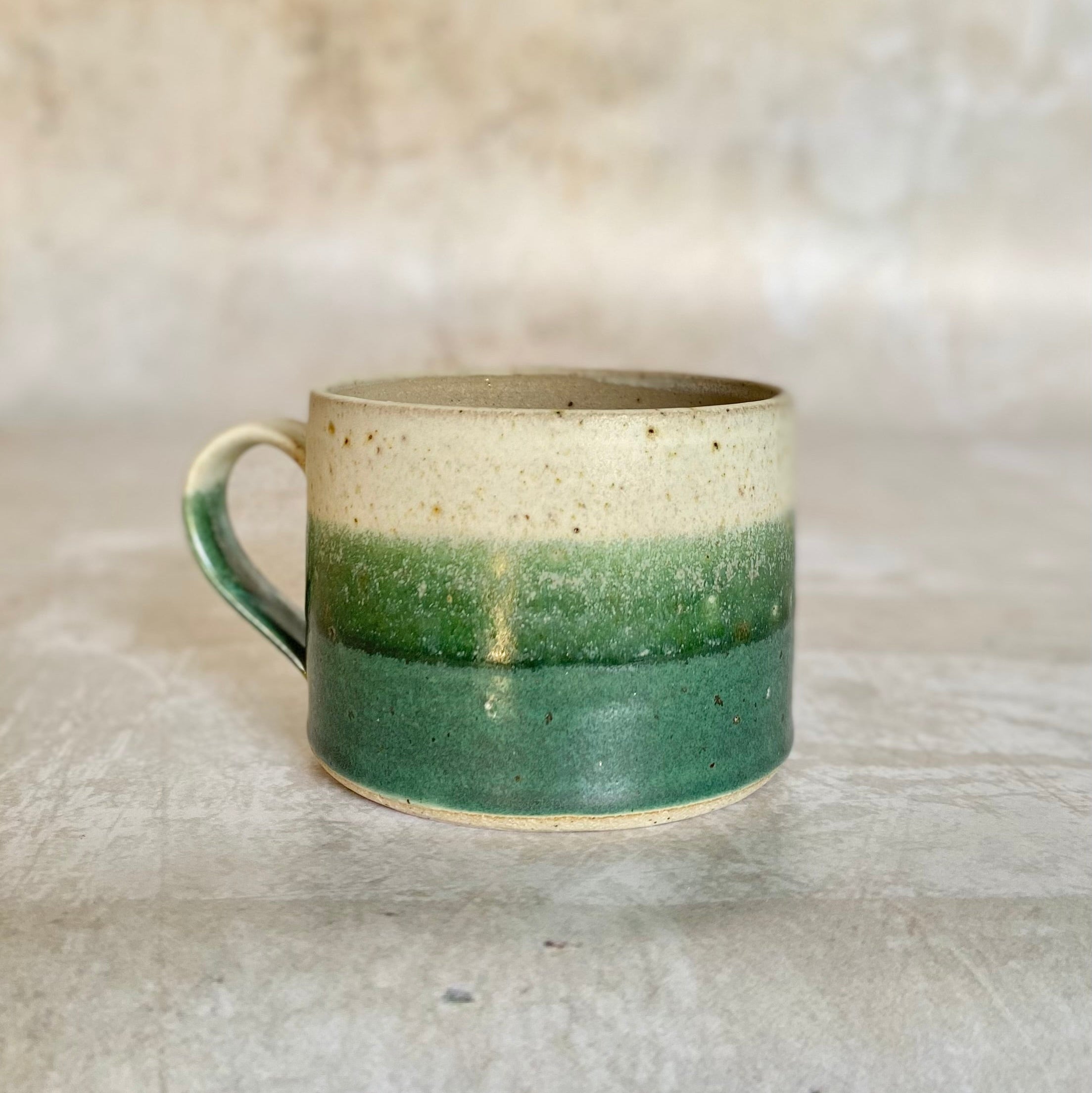 Stoneware mug with a speckled off-white top, a creamy midsection, and a deep green bottom.