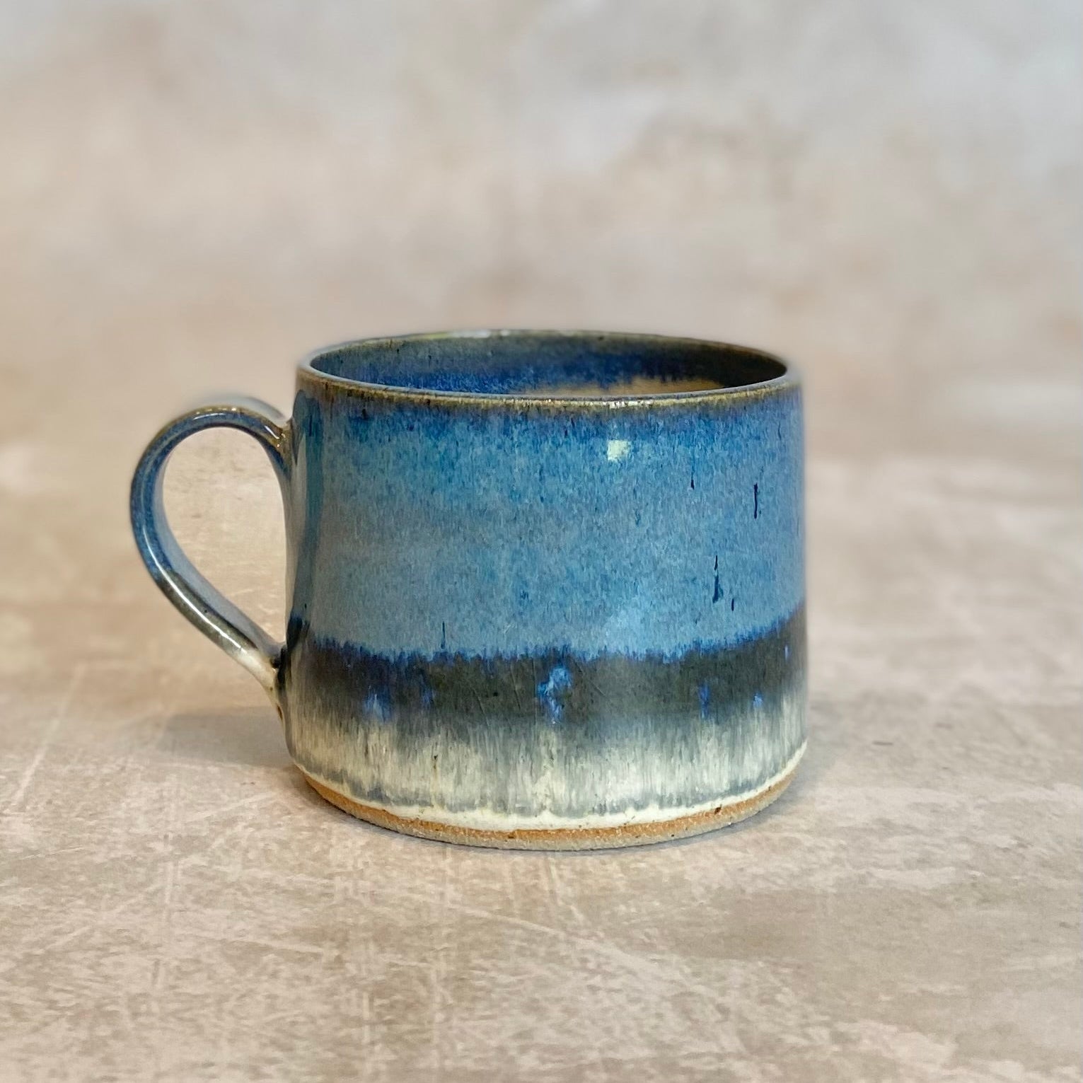 Hand-thrown stoneware mug with a blue-toned glaze, featuring darker blue and off-white banding near the base.