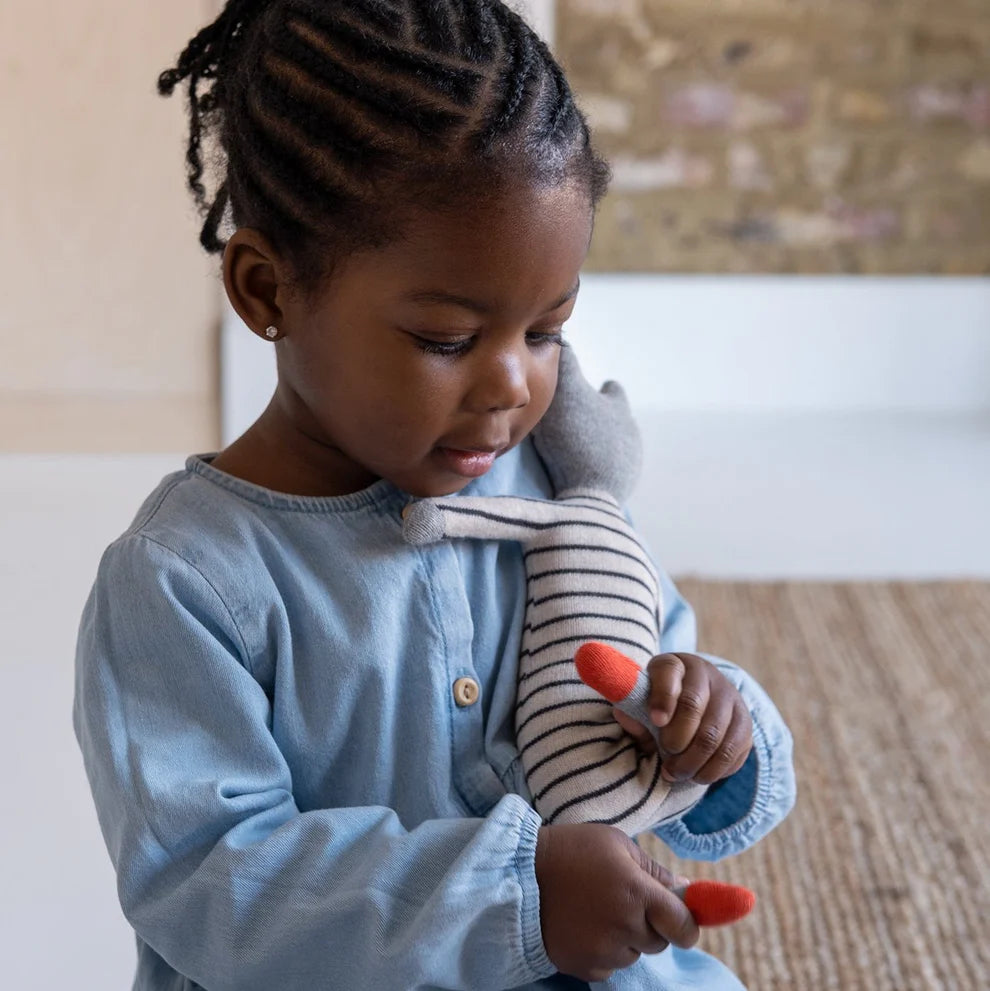 A toddler in a light blue shirt holds a small striped stuffed animal with orange accents.